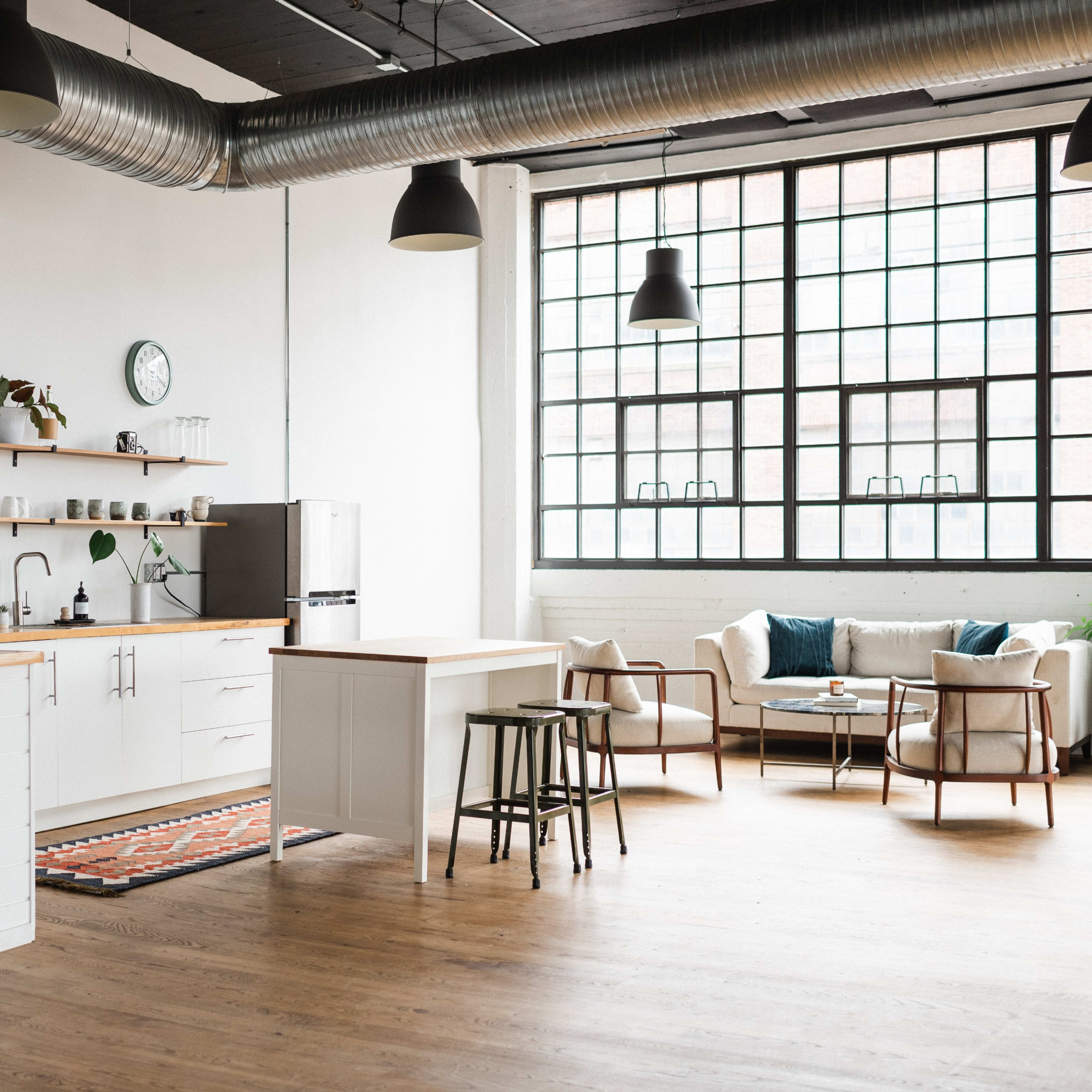 A modern kitchen and living area with wooden floors, a large window, and minimalist furnishings.