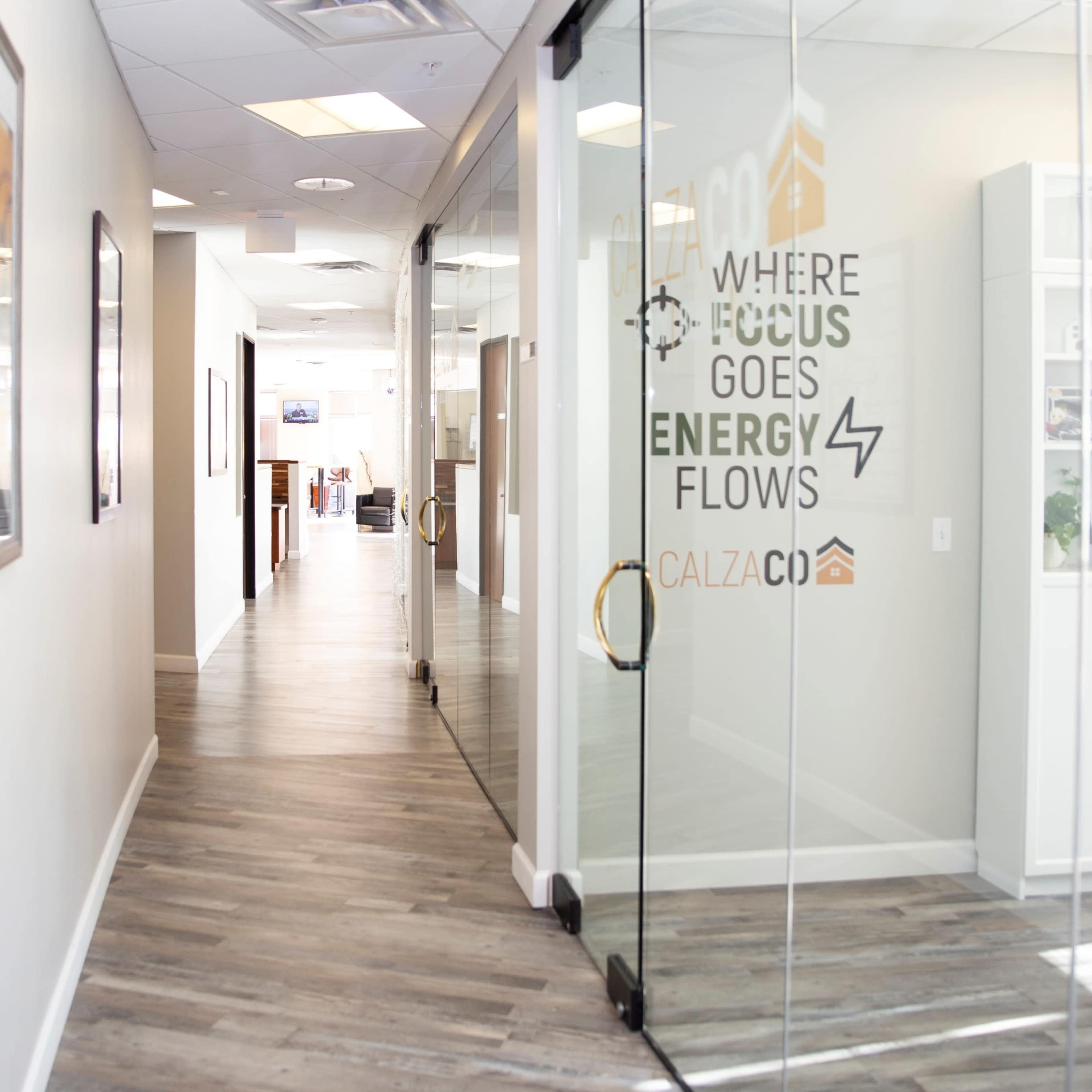 A long, well-lit hallway with glass doors leads to an office workspace, featuring modern decor and a motivational message on the wall.