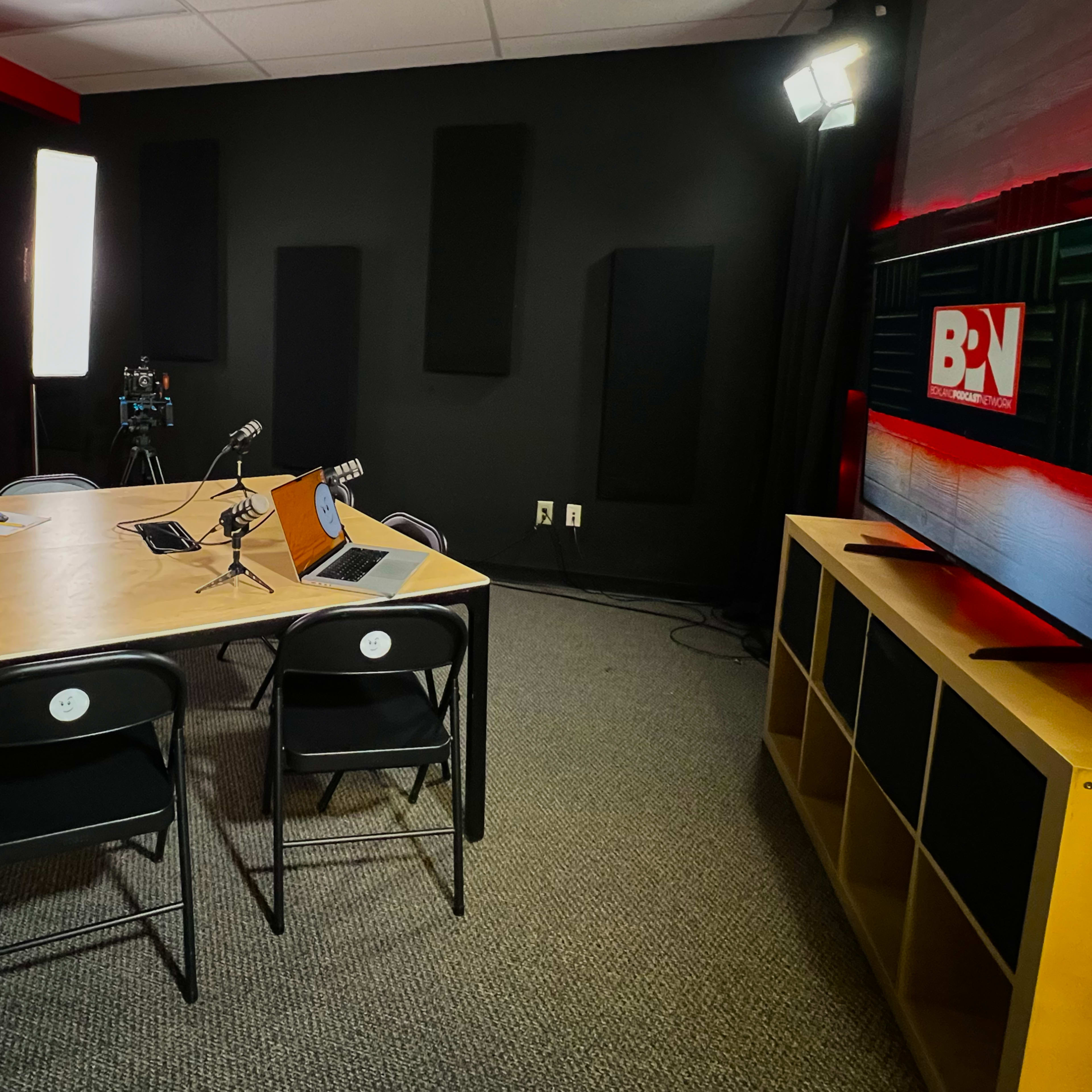 A modern recording studio with a central table, two chairs, cameras on tripods, and soundproofing panels on the walls.