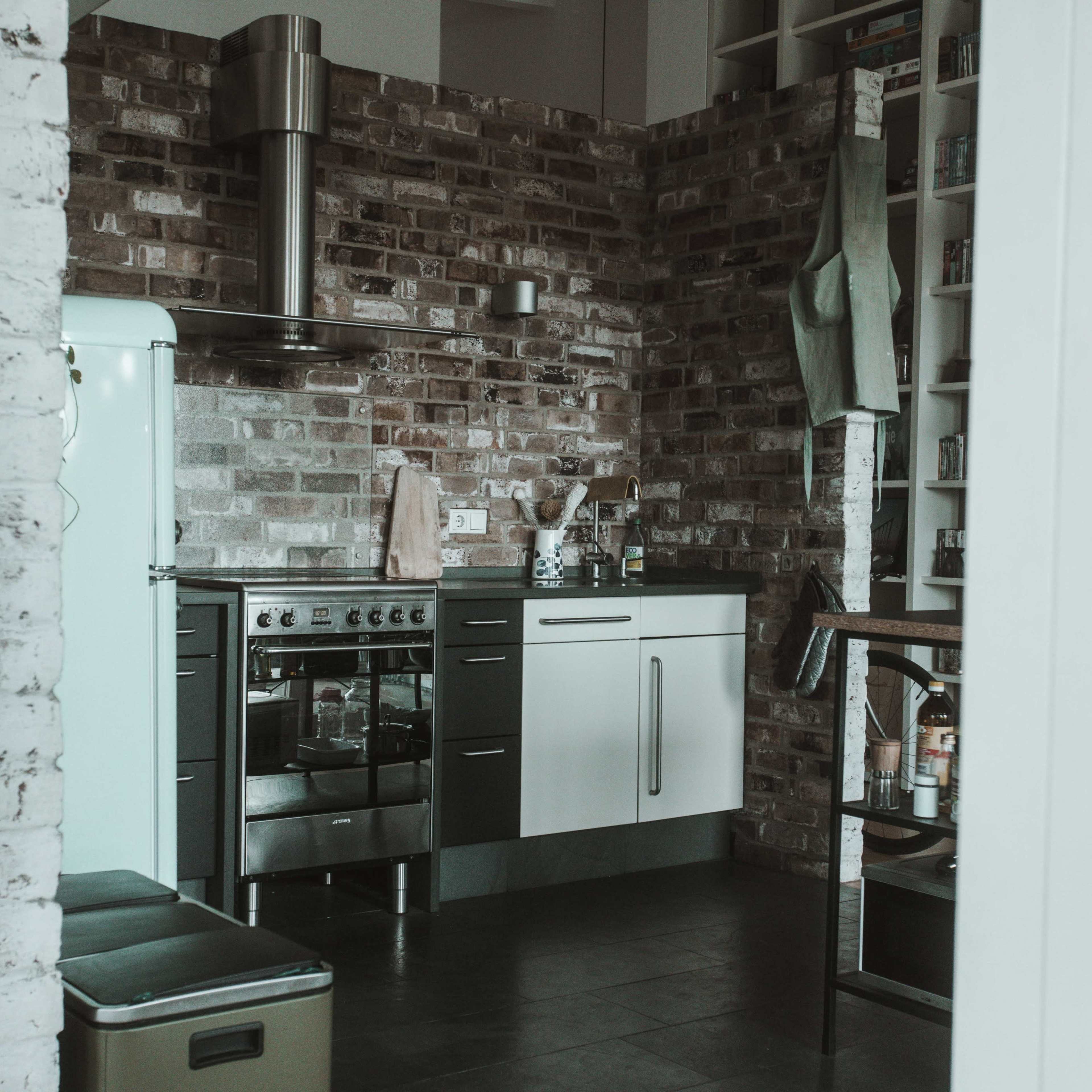 A kitchen featuring a stainless steel stove, an old-fashioned refrigerator, and exposed brick walls.