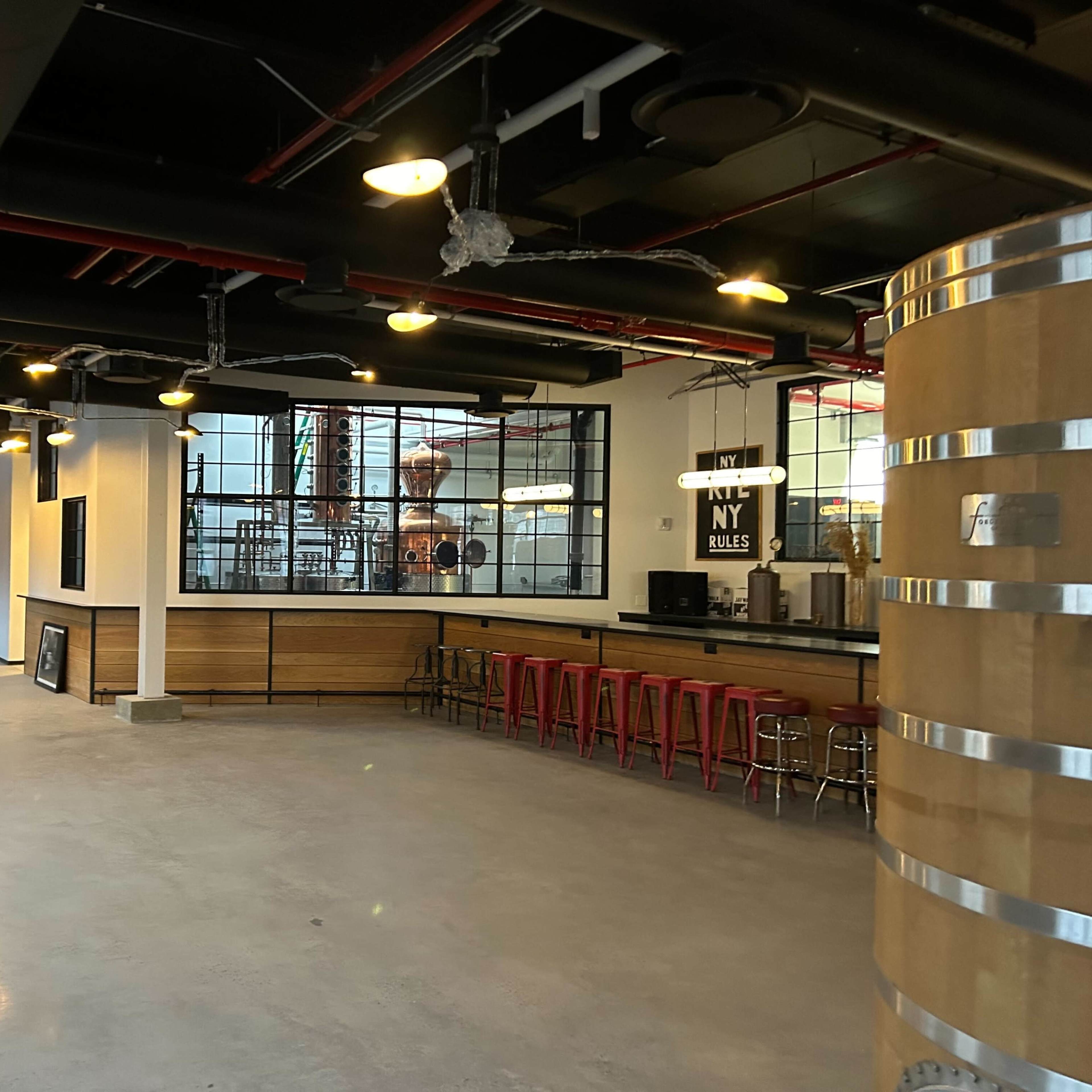 A spacious, industrial-style interior featuring a bar with red stools, large windows, and wooden paneling.