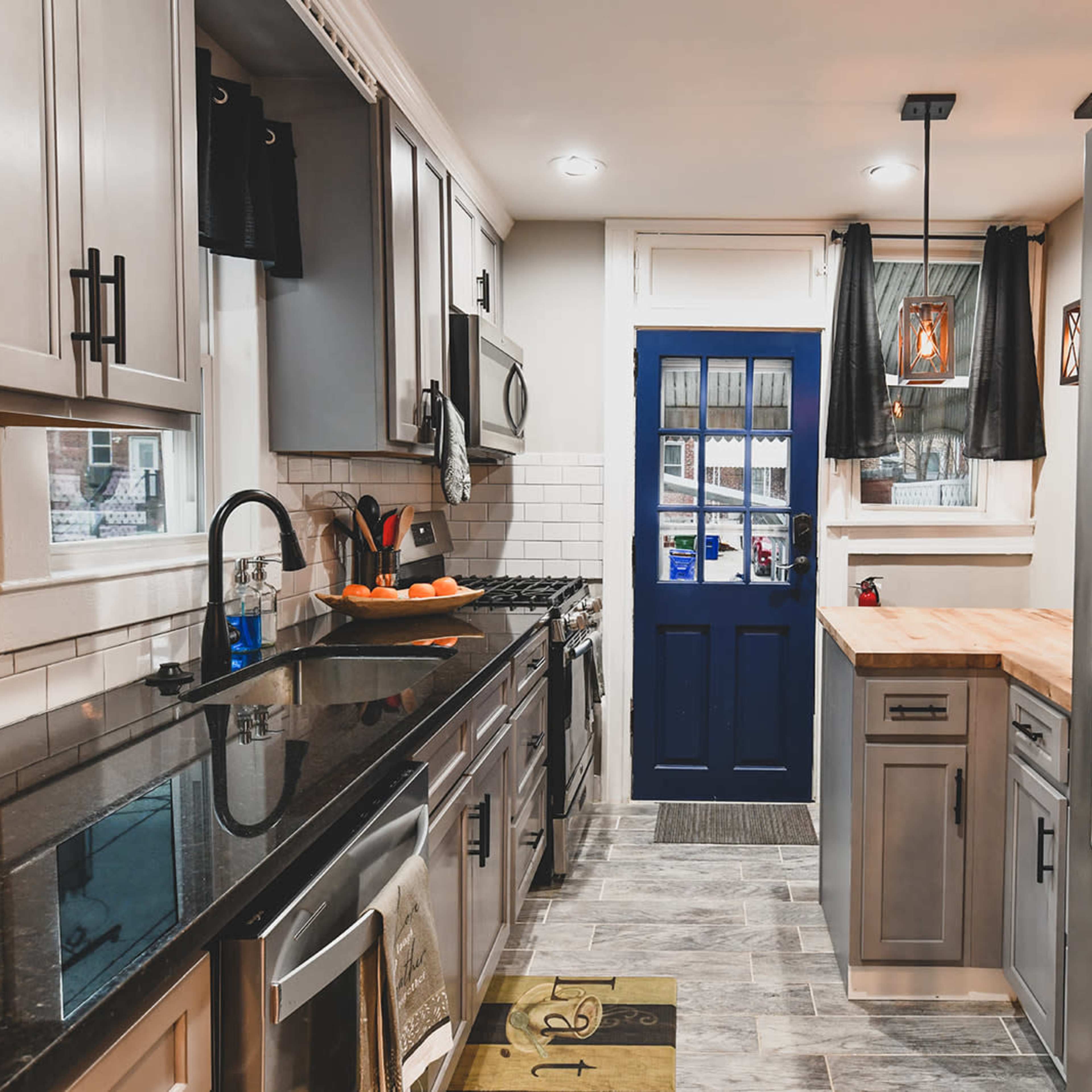A modern kitchen with stainless steel appliances, dark countertops, and a blue door leading outside.