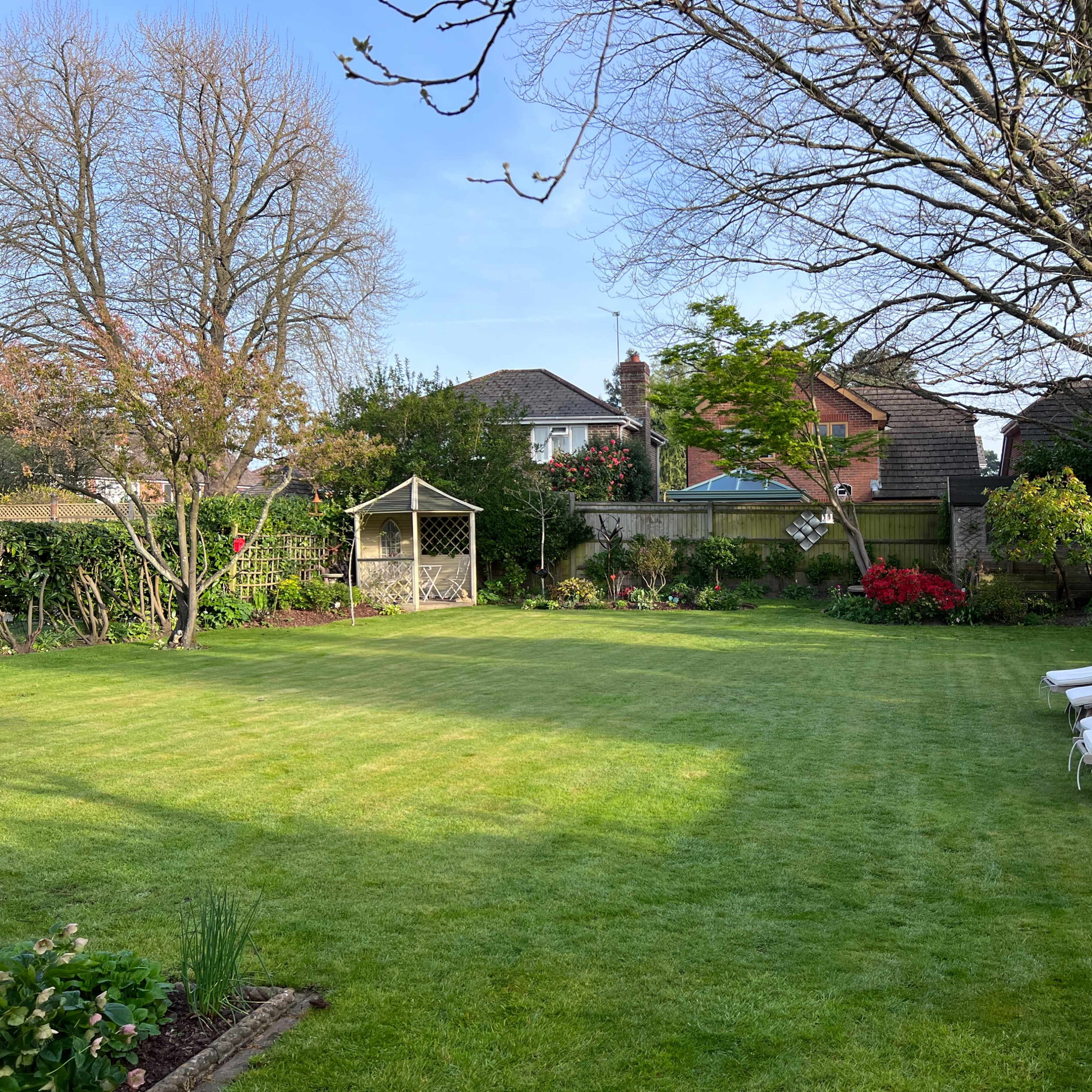 A manicured garden with neatly trimmed grass, a gazebo, and lounge chairs arranged on one side.