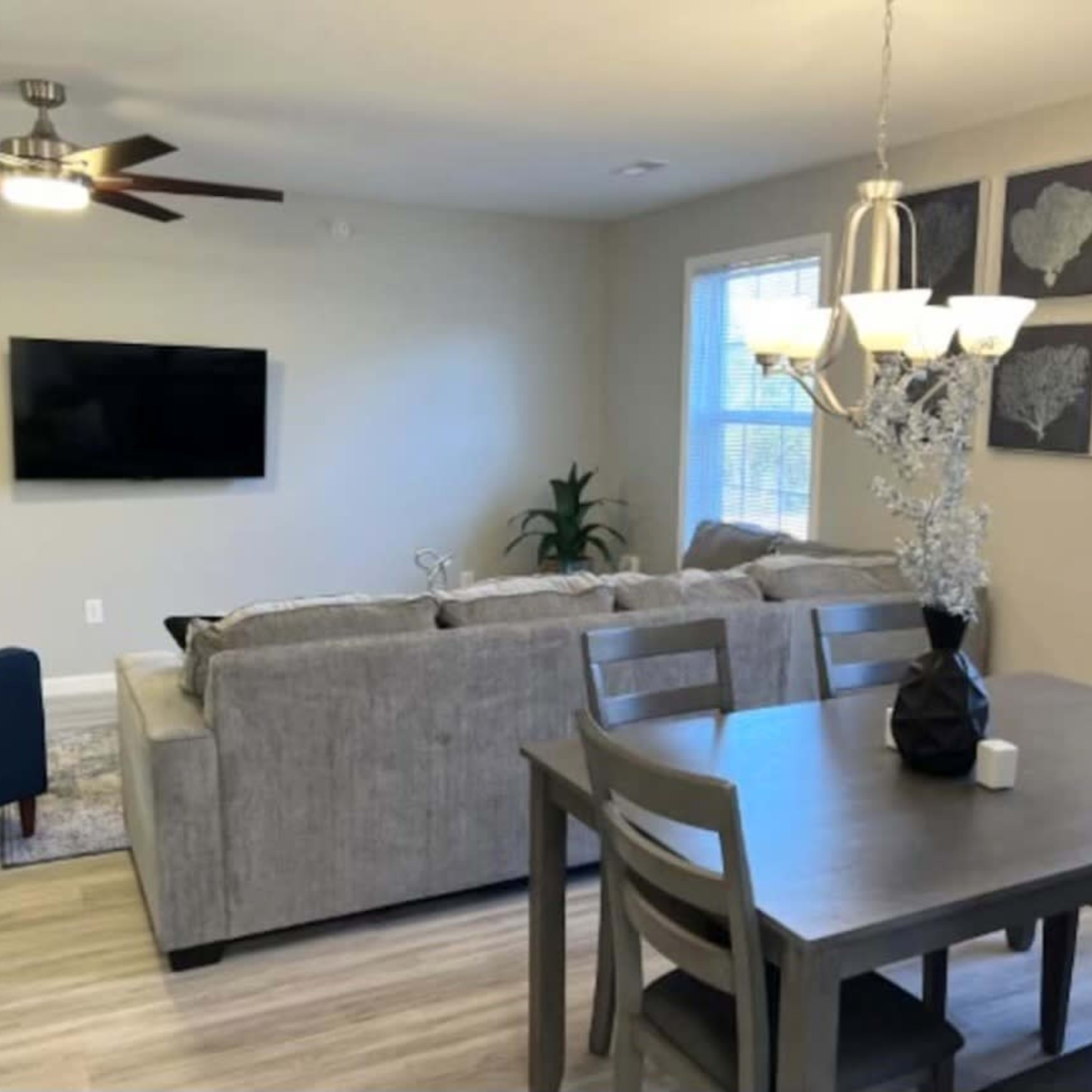 A living and dining area with a gray sectional sofa, a wooden dining table with chairs, and a wall-mounted television.