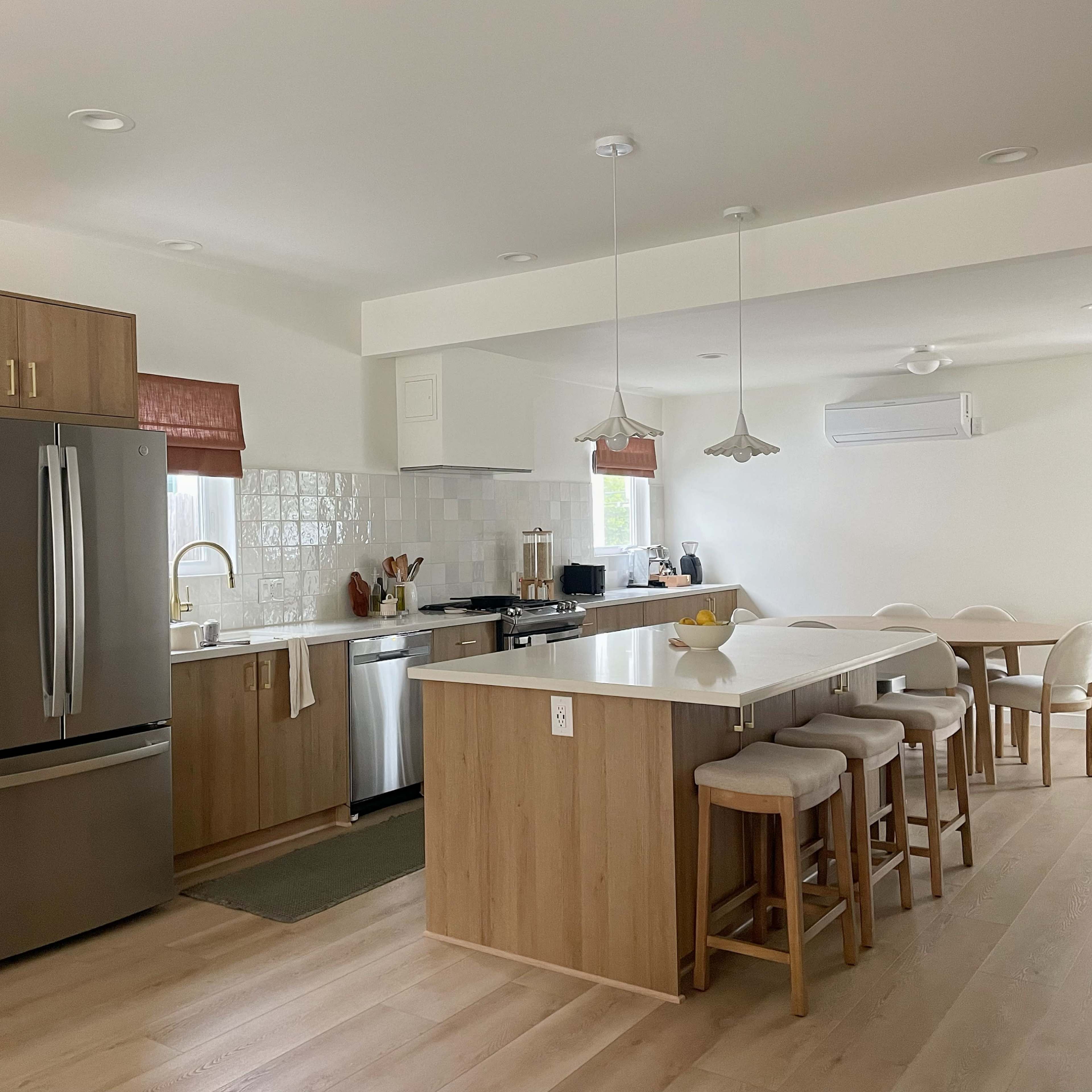 A modern kitchen featuring wooden cabinetry, stainless steel appliances, and a dining area with a round table and chairs.