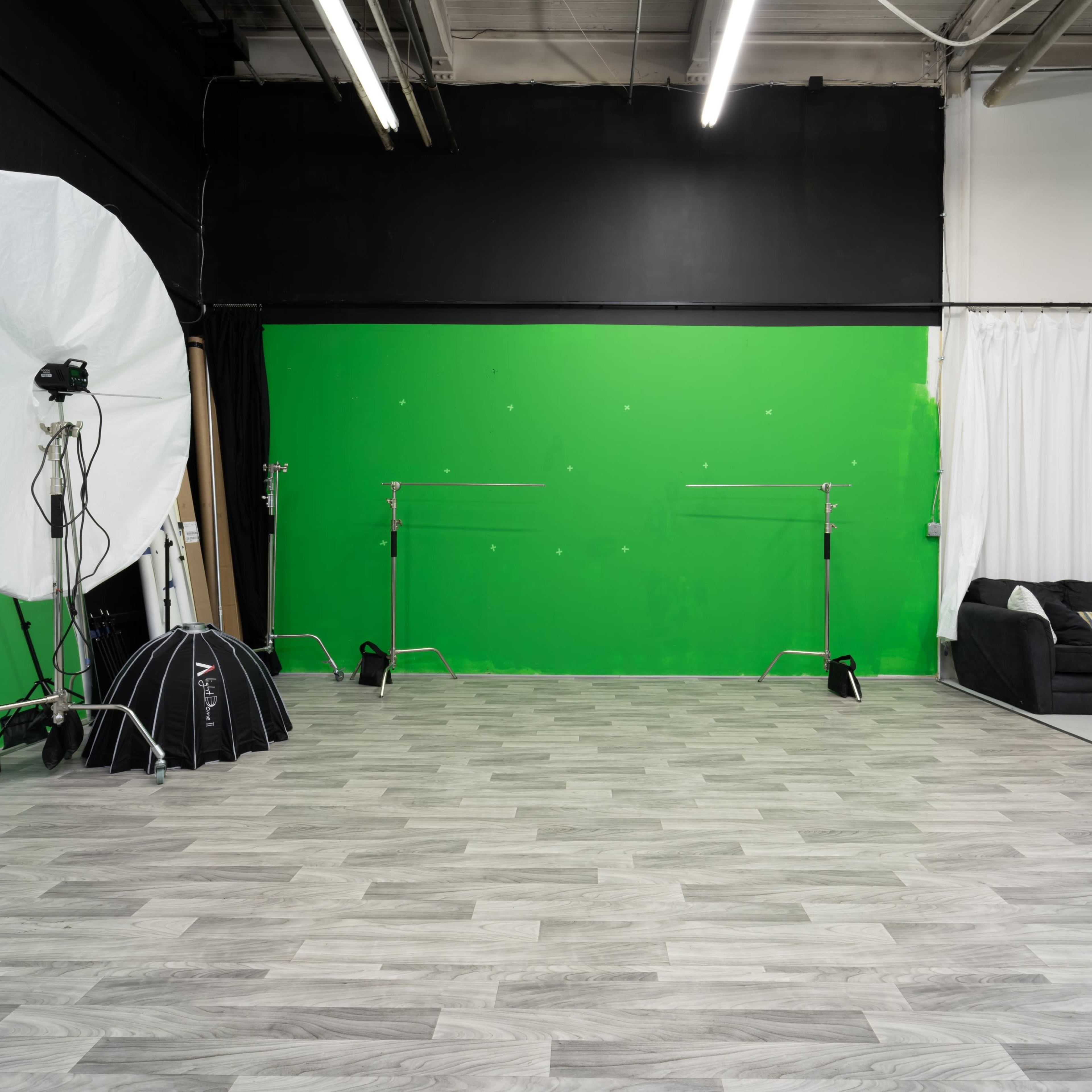 A photography studio features a green screen backdrop, lighting equipment, and a sofa against a wall.