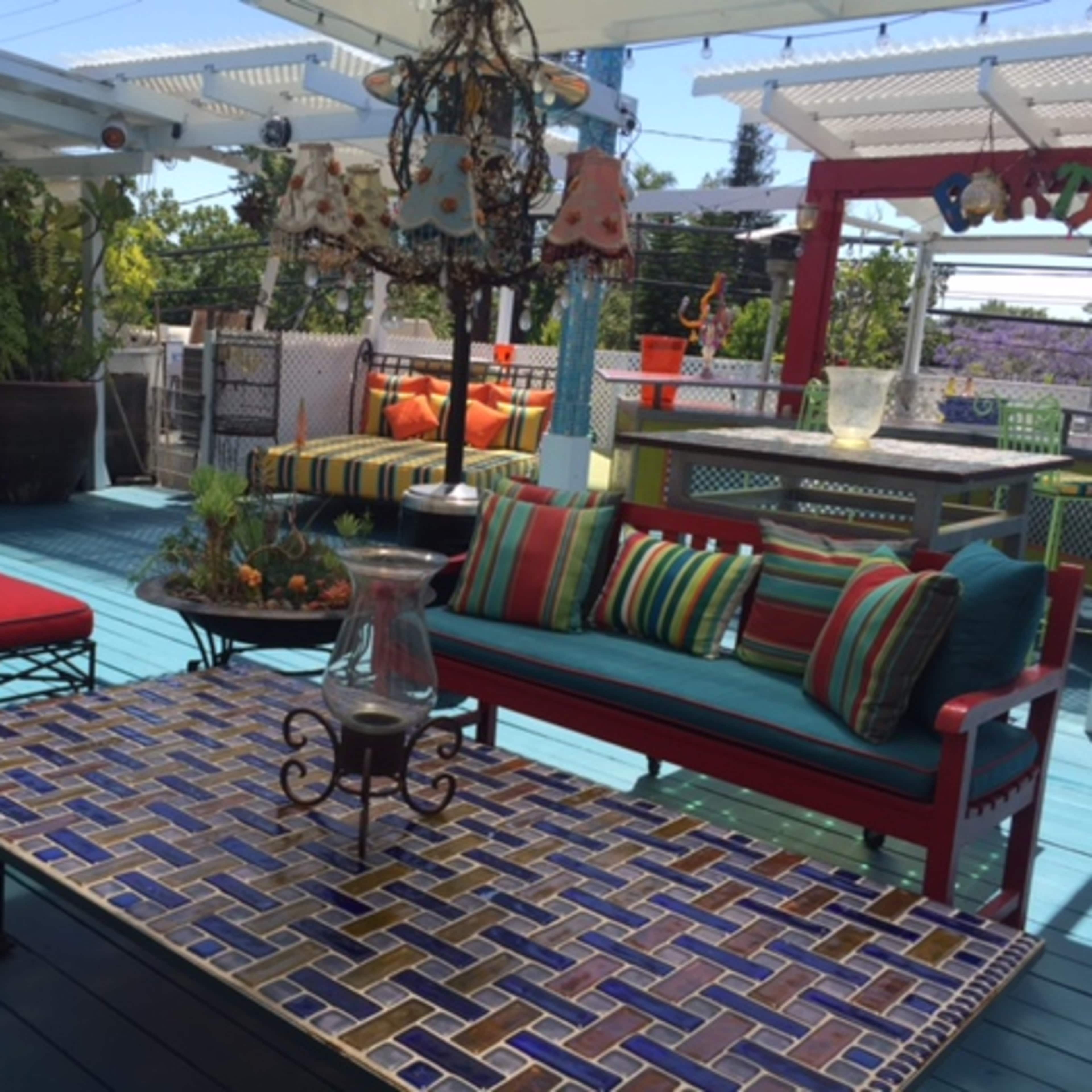 A vibrant outdoor space features colorful seating and a decorative tiled coffee table surrounded by greenery.