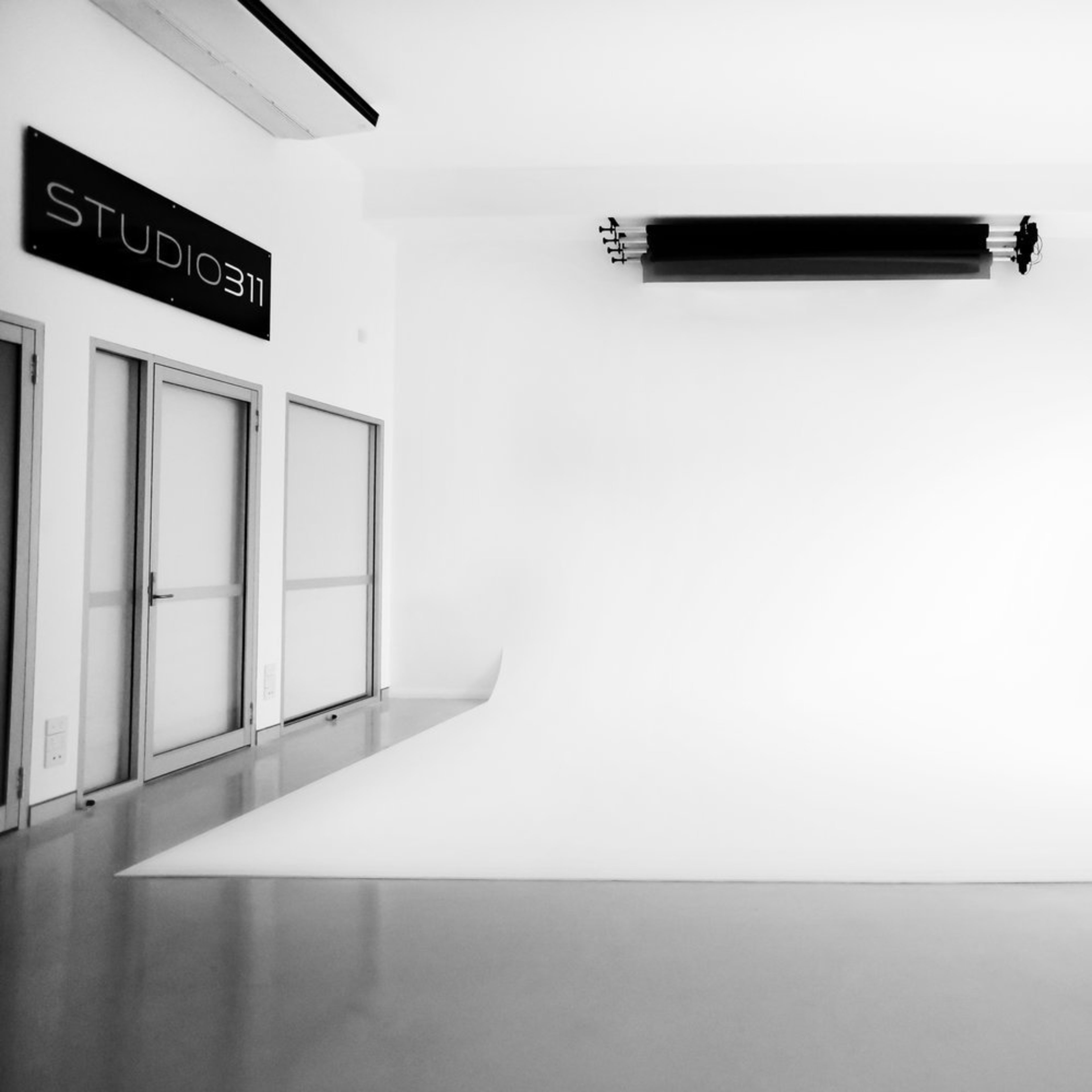 A spacious, minimalist photography studio with a white backdrop and large windows.