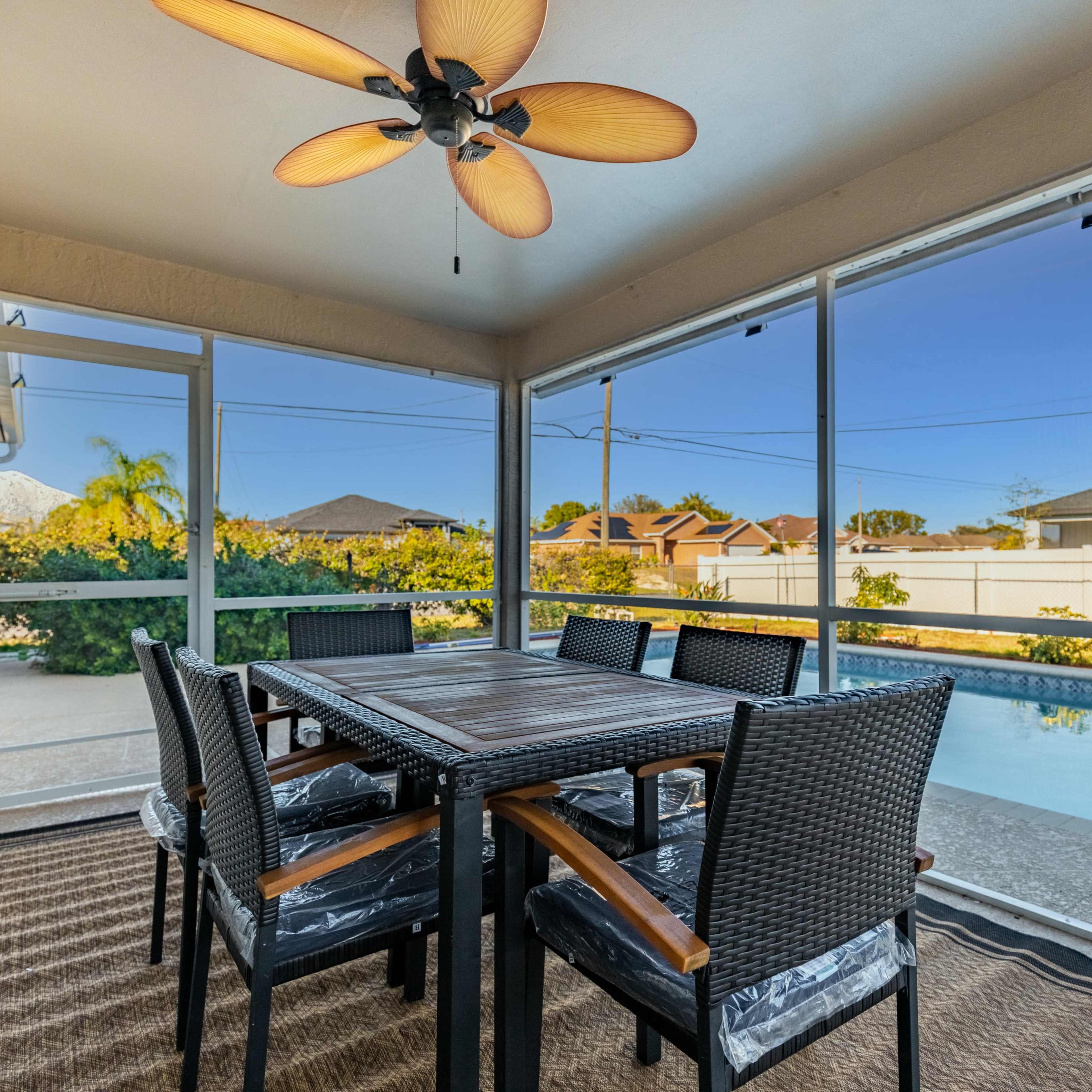 A screened-in patio features a dining table with six chairs, overlooking a swimming pool surrounded by greenery.