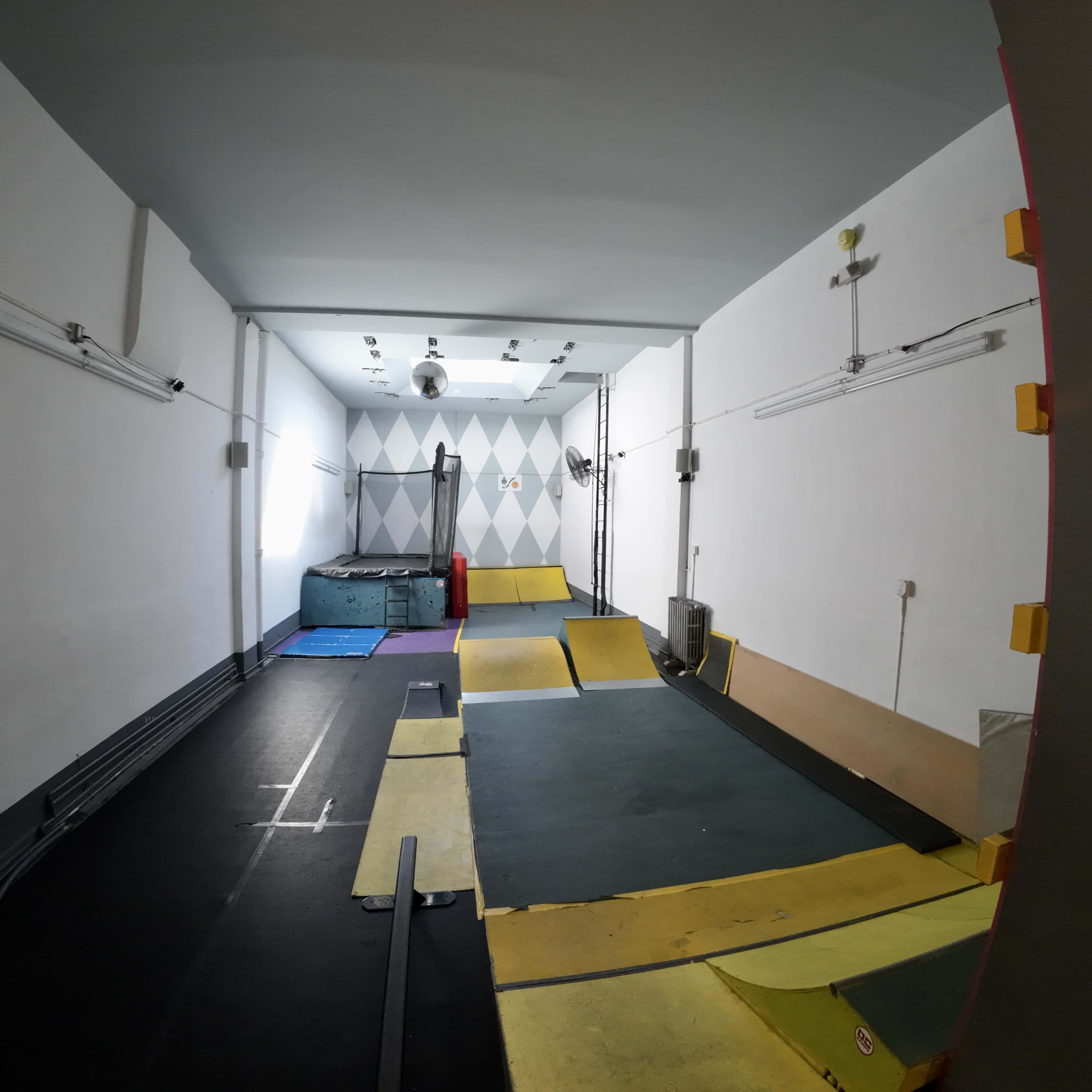 A small indoor space designed for parkour training, featuring ramps, mats, and a colorful geometric wall.
