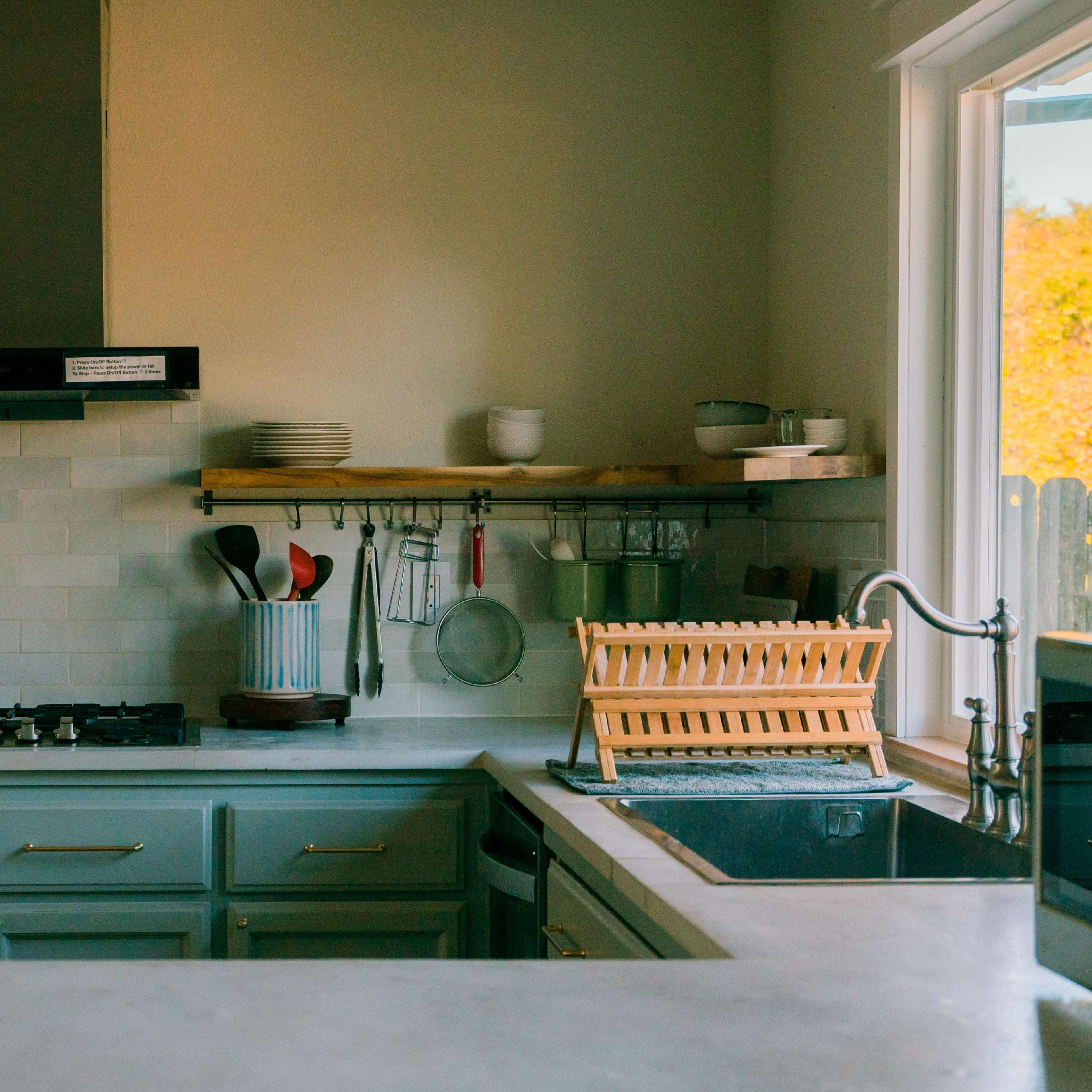 A modern kitchen with a gas stove, wooden shelves holding dishes, and a dish rack near the sink.