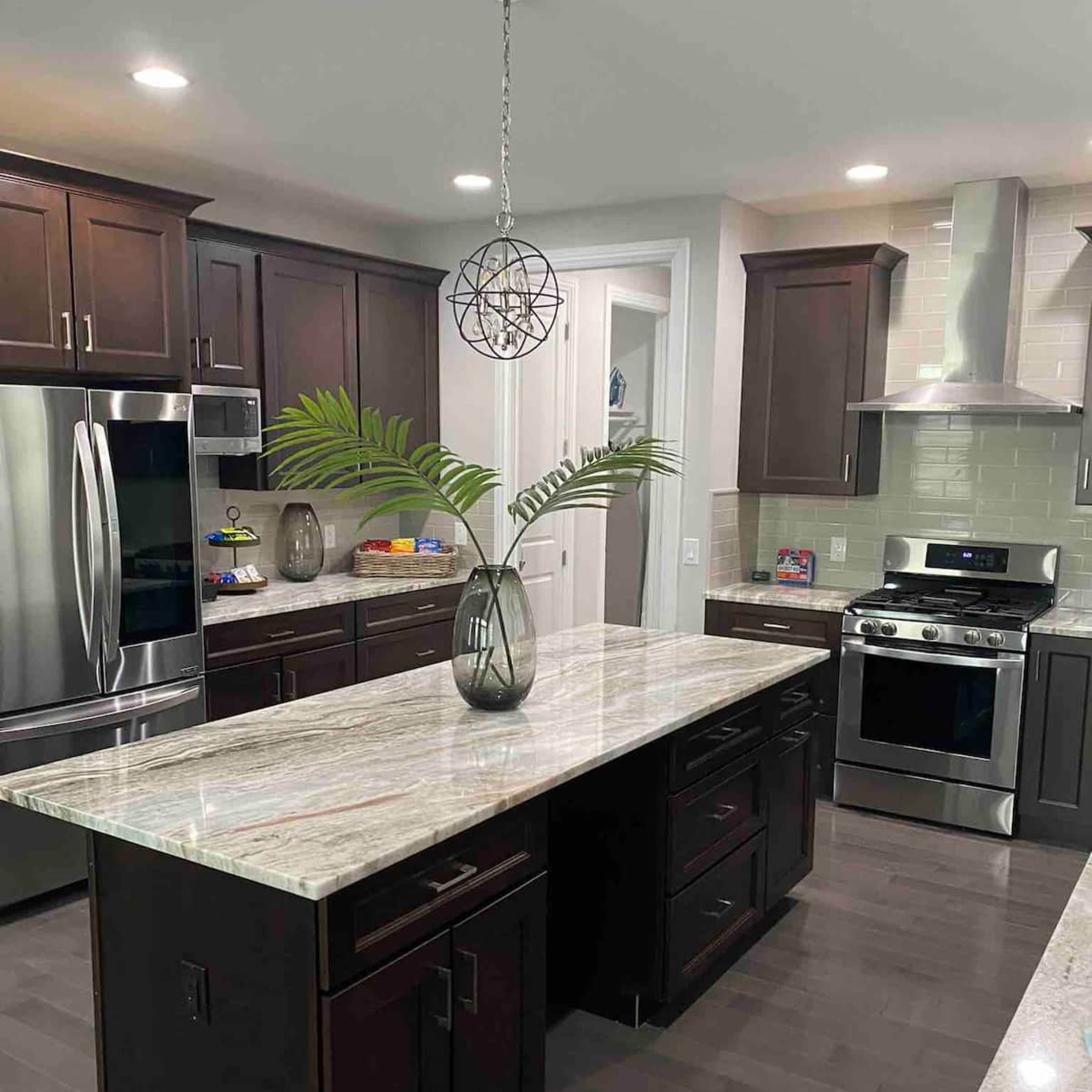 A modern kitchen features dark wooden cabinets, a large island with a marble countertop, and stainless steel appliances.