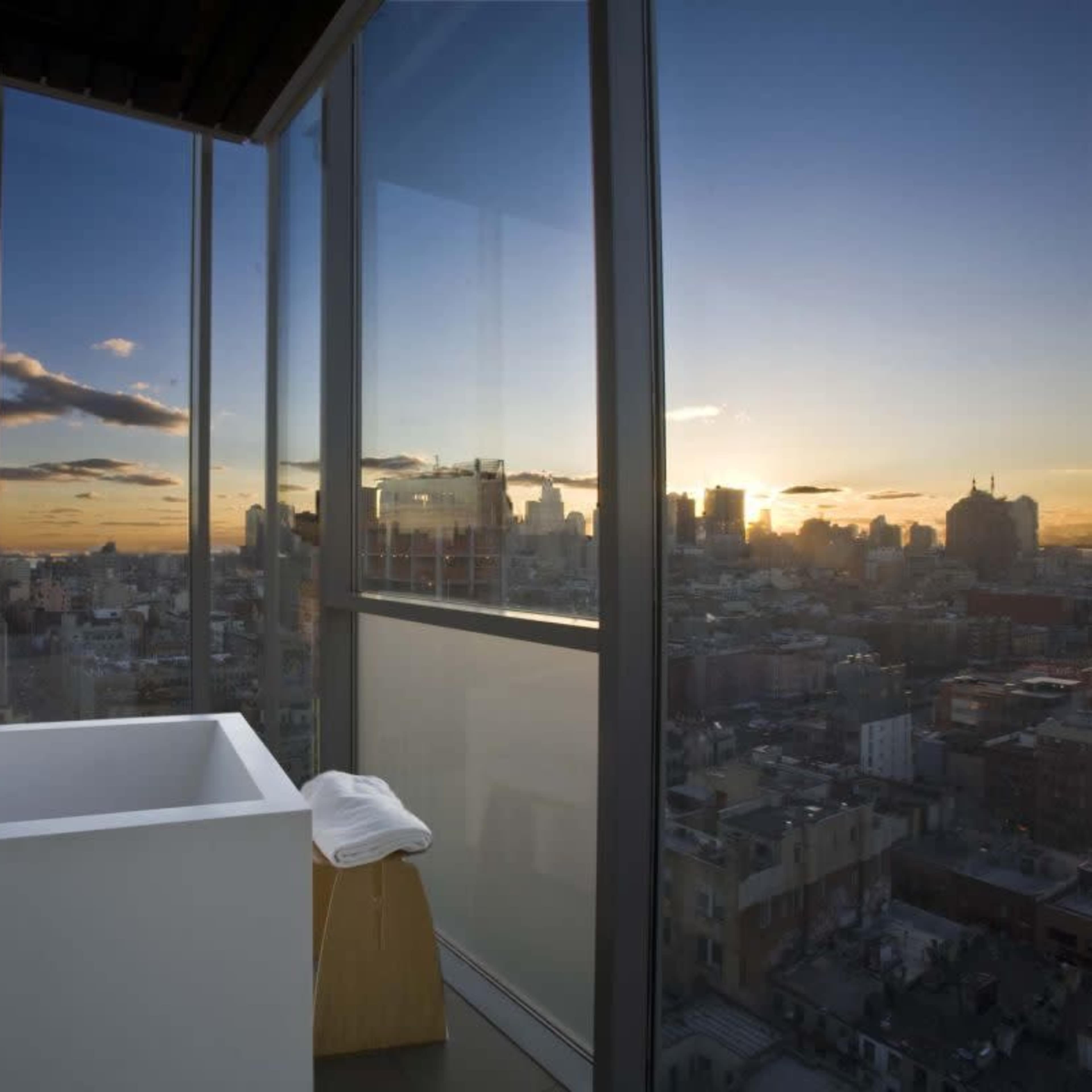 A modern bathroom features a freestanding tub beside large windows showcasing a city skyline at sunset.