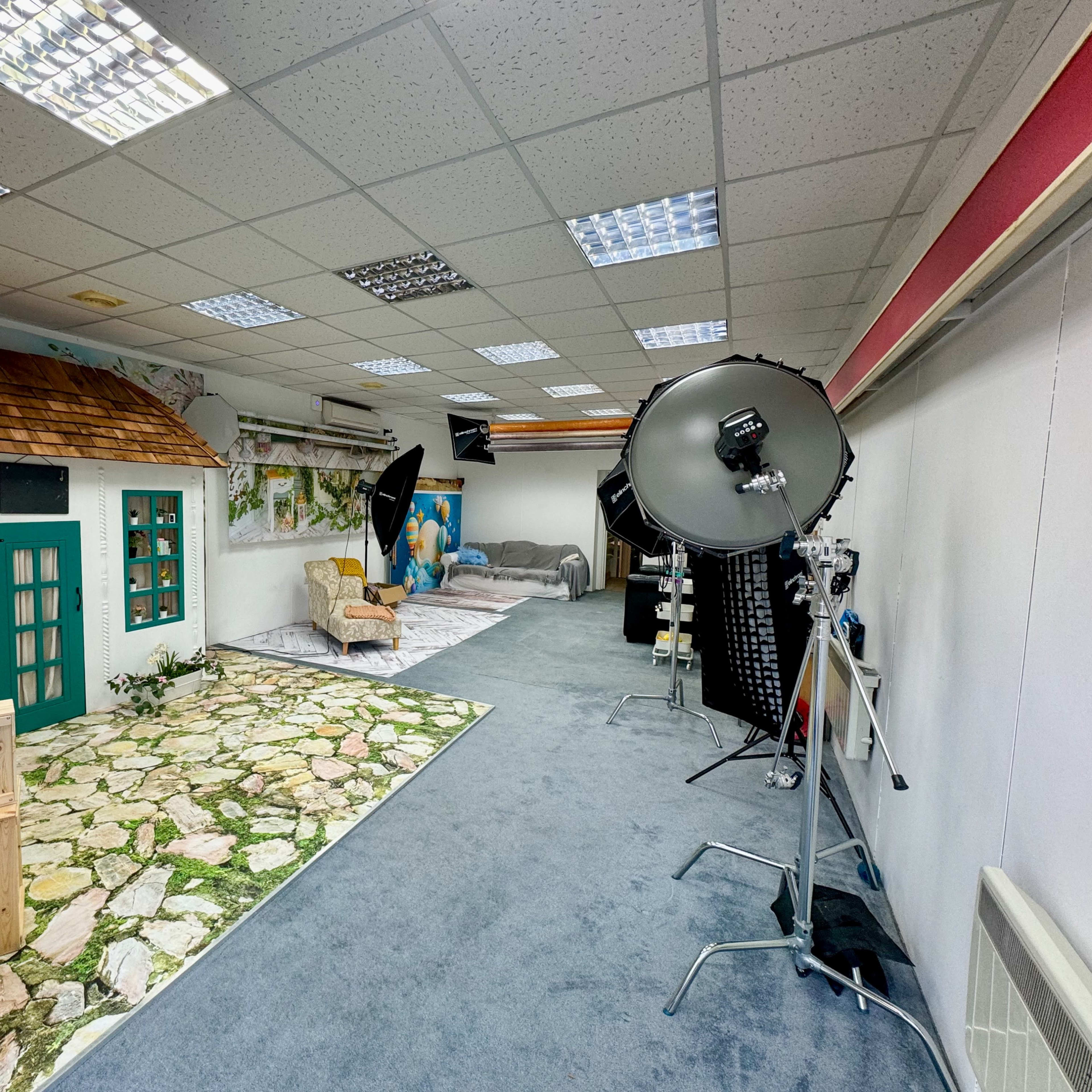 A photography studio featuring a faux cottage interior with a stone pathway and multiple lighting setups.