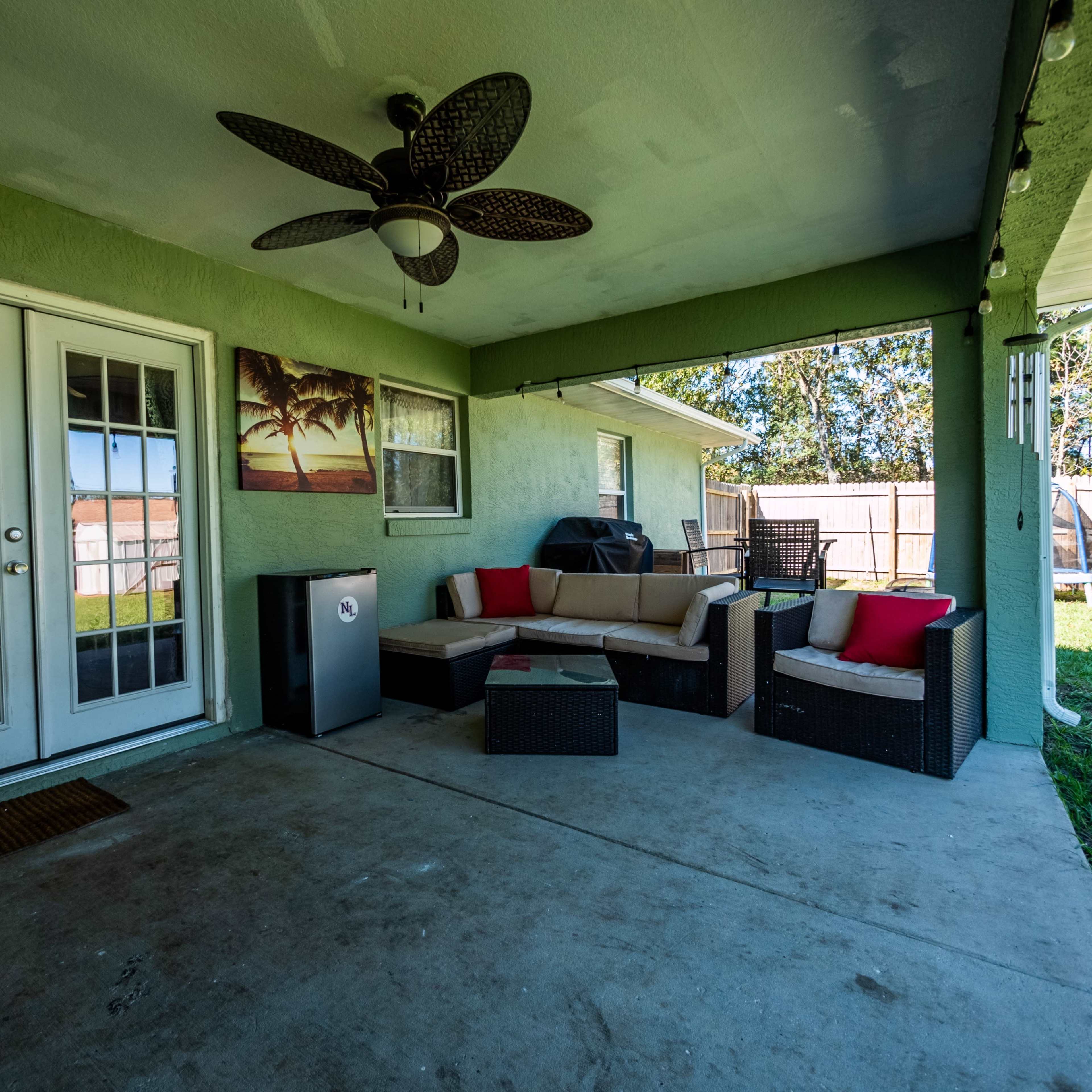 A covered patio with a seating area featuring a couch and chairs, a grill in the corner, and double doors leading to the interior of a house.