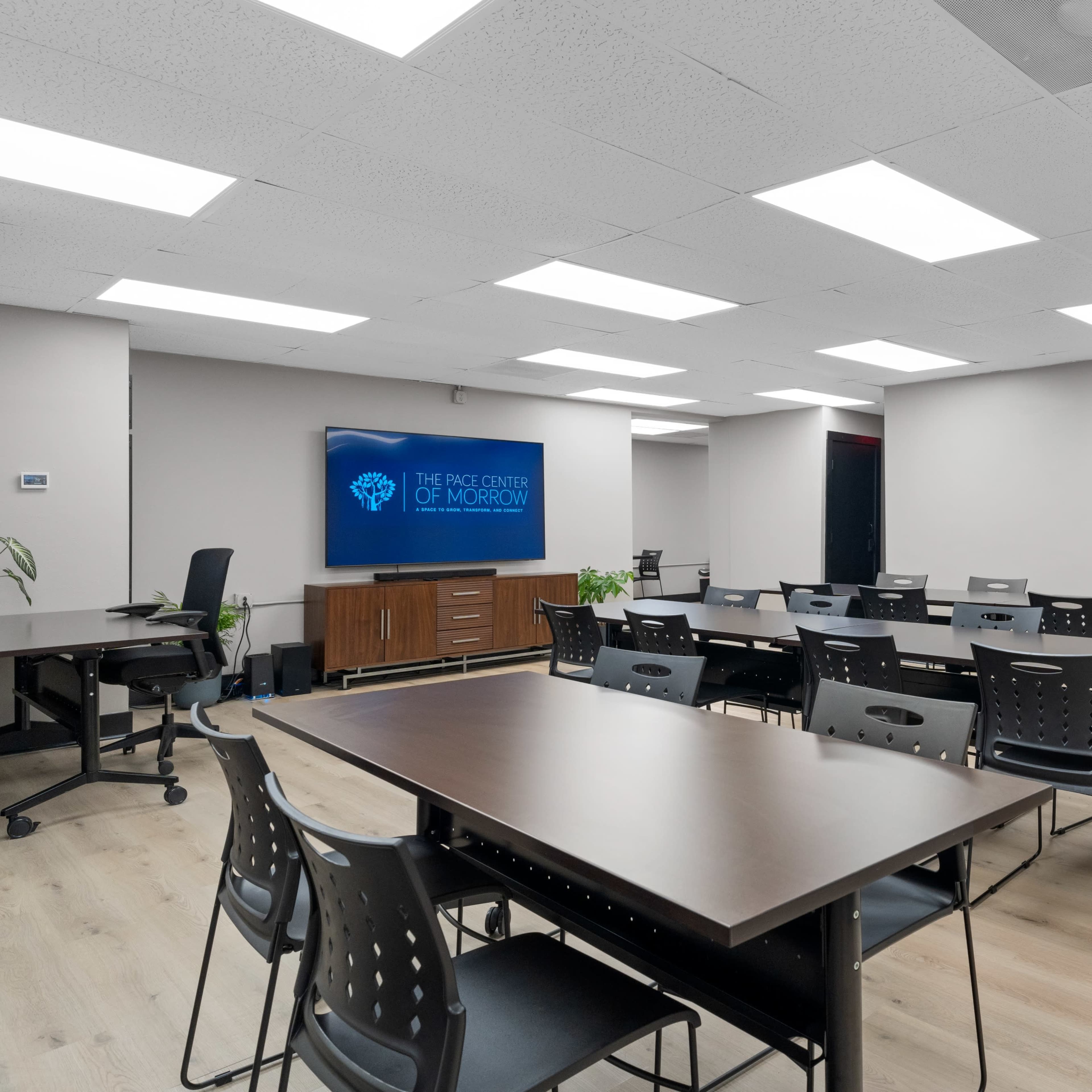 A modern classroom setup with rows of tables and chairs, featuring a large screen displaying "The Pace Center of Morrow" on one wall.