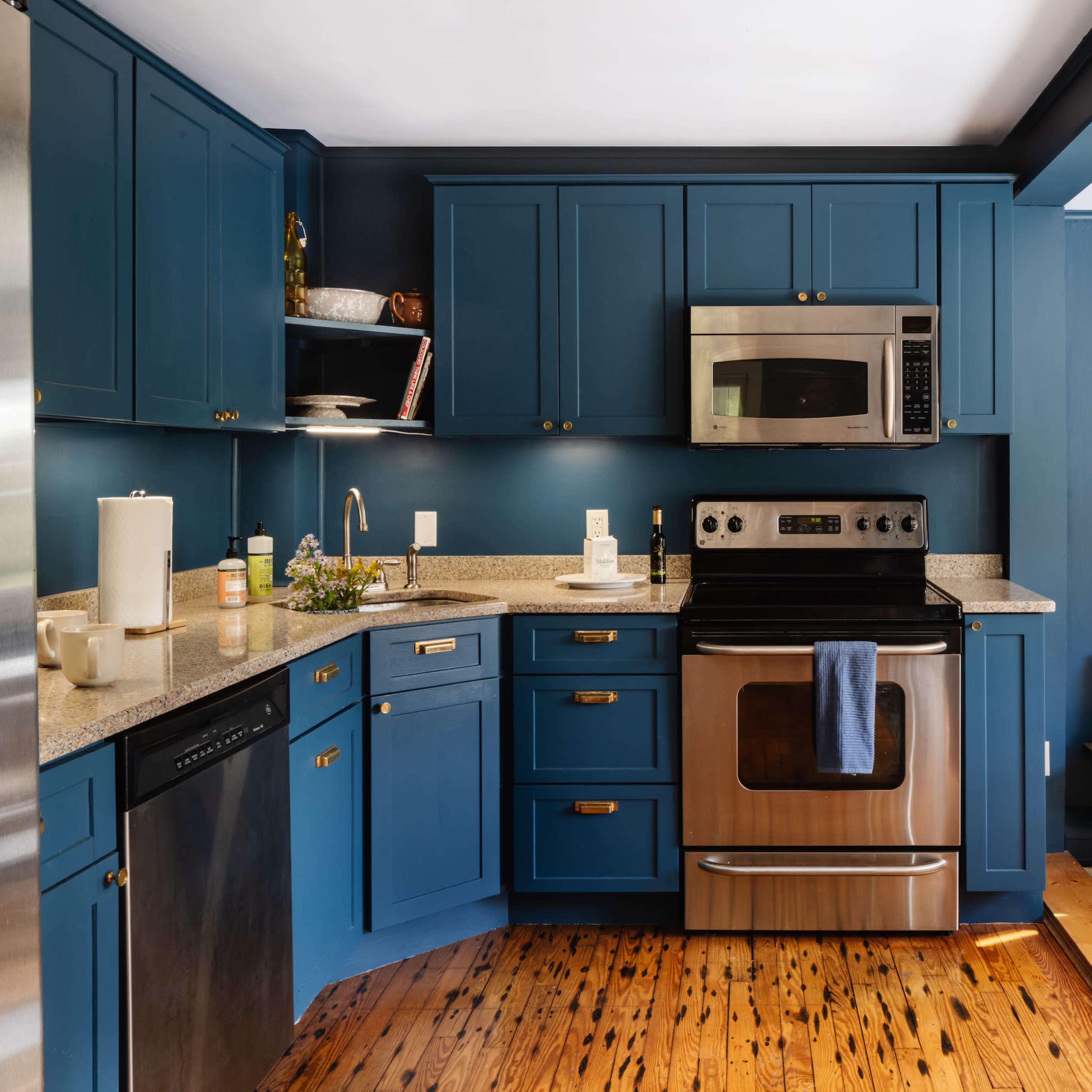 A modern kitchen with blue cabinets, stainless steel appliances, and wooden floors.