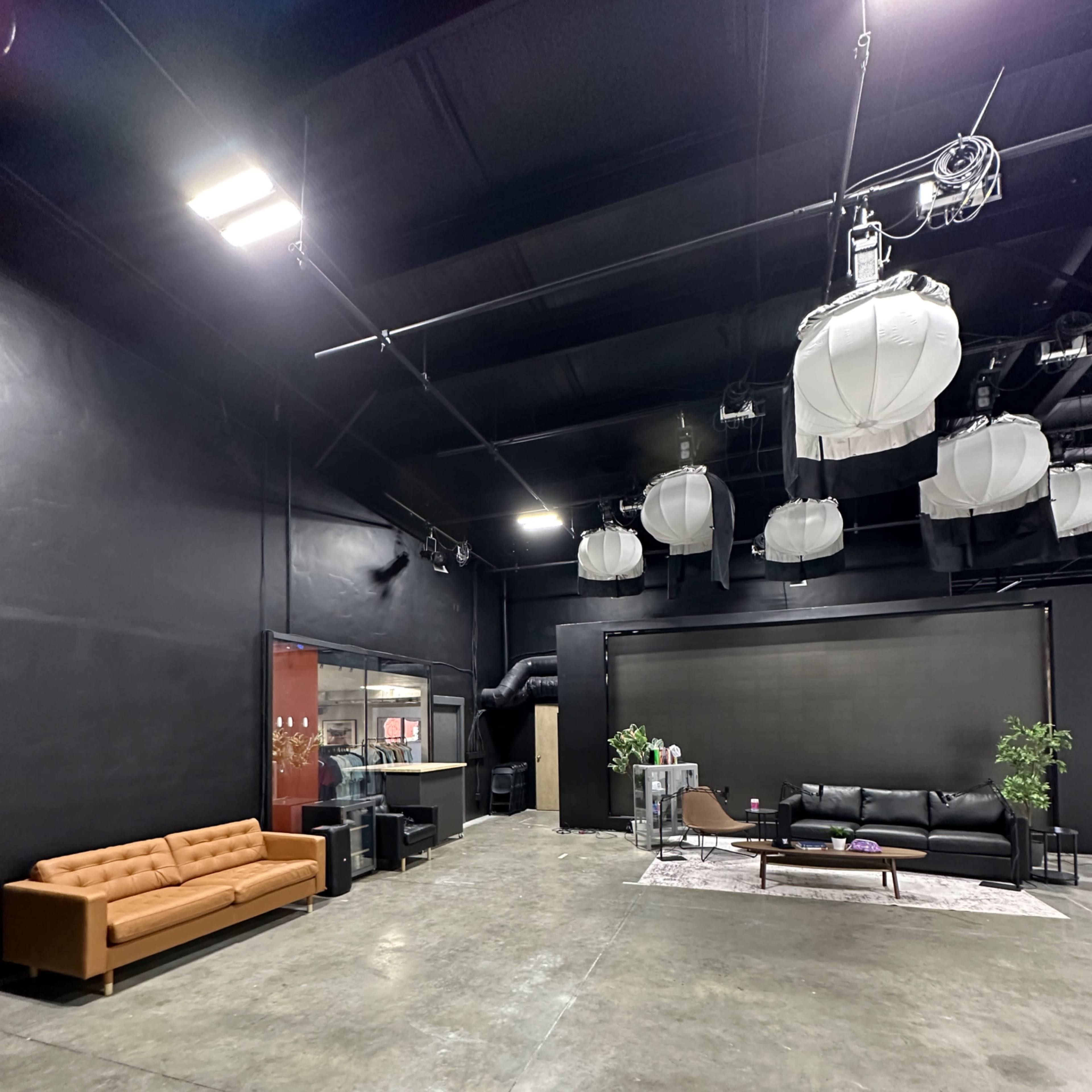 A large black-walled studio space featuring two sofas, a coffee table, and hanging light fixtures.