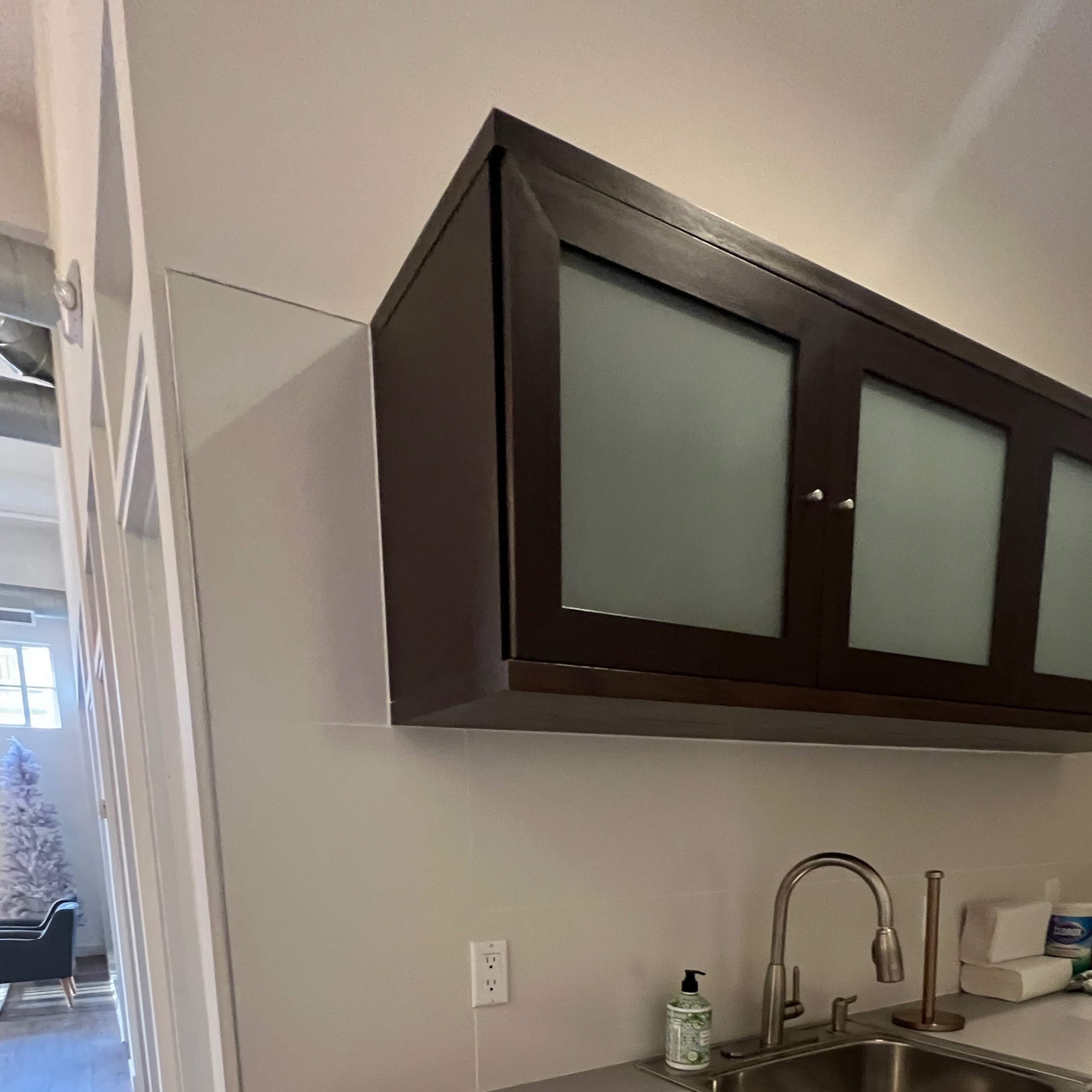 A modern kitchen with a sink and cabinet above a counter, leading to a hallway at the back.