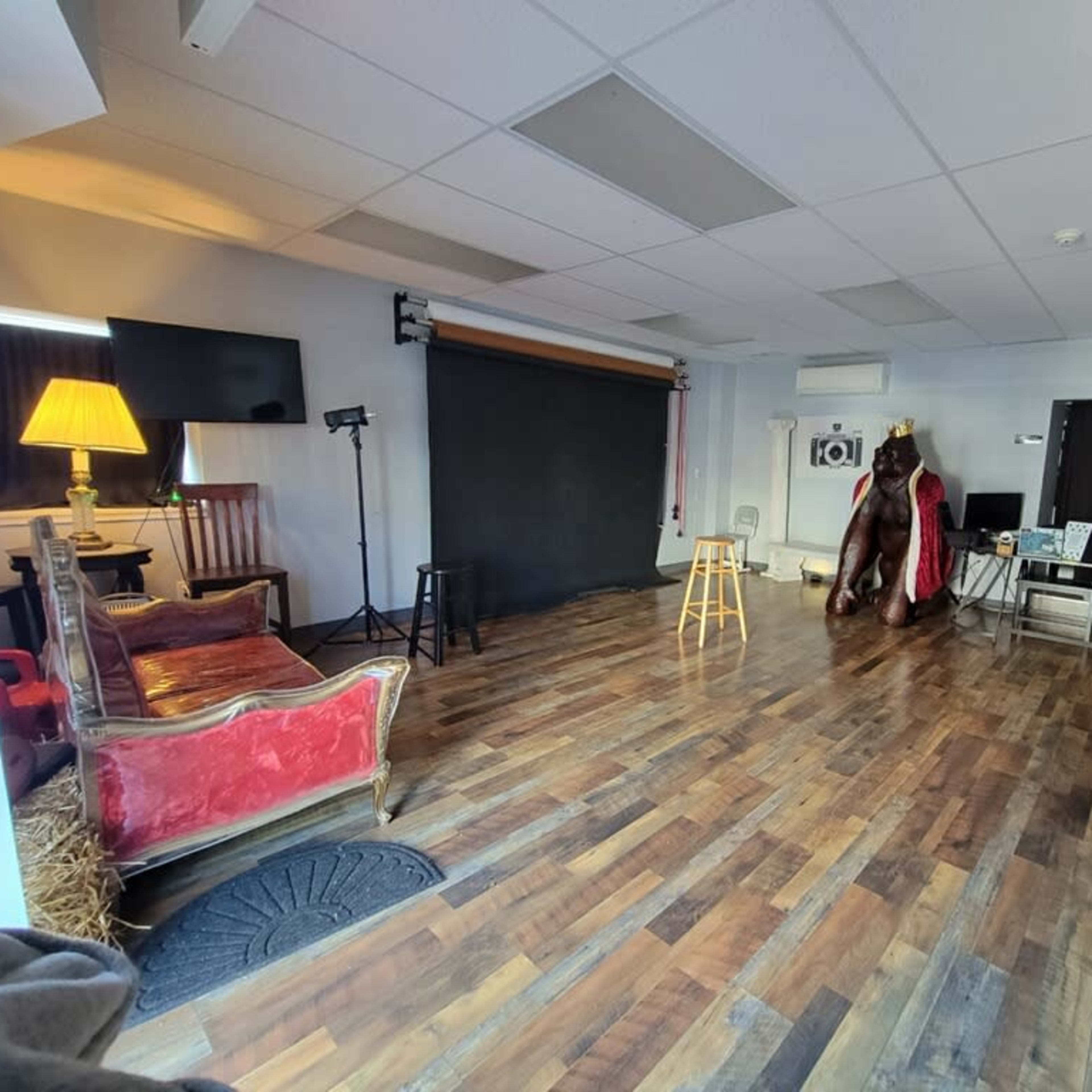 A spacious studio with wooden flooring, a black backdrop, a stool, several seating areas, and various equipment arranged around the room.