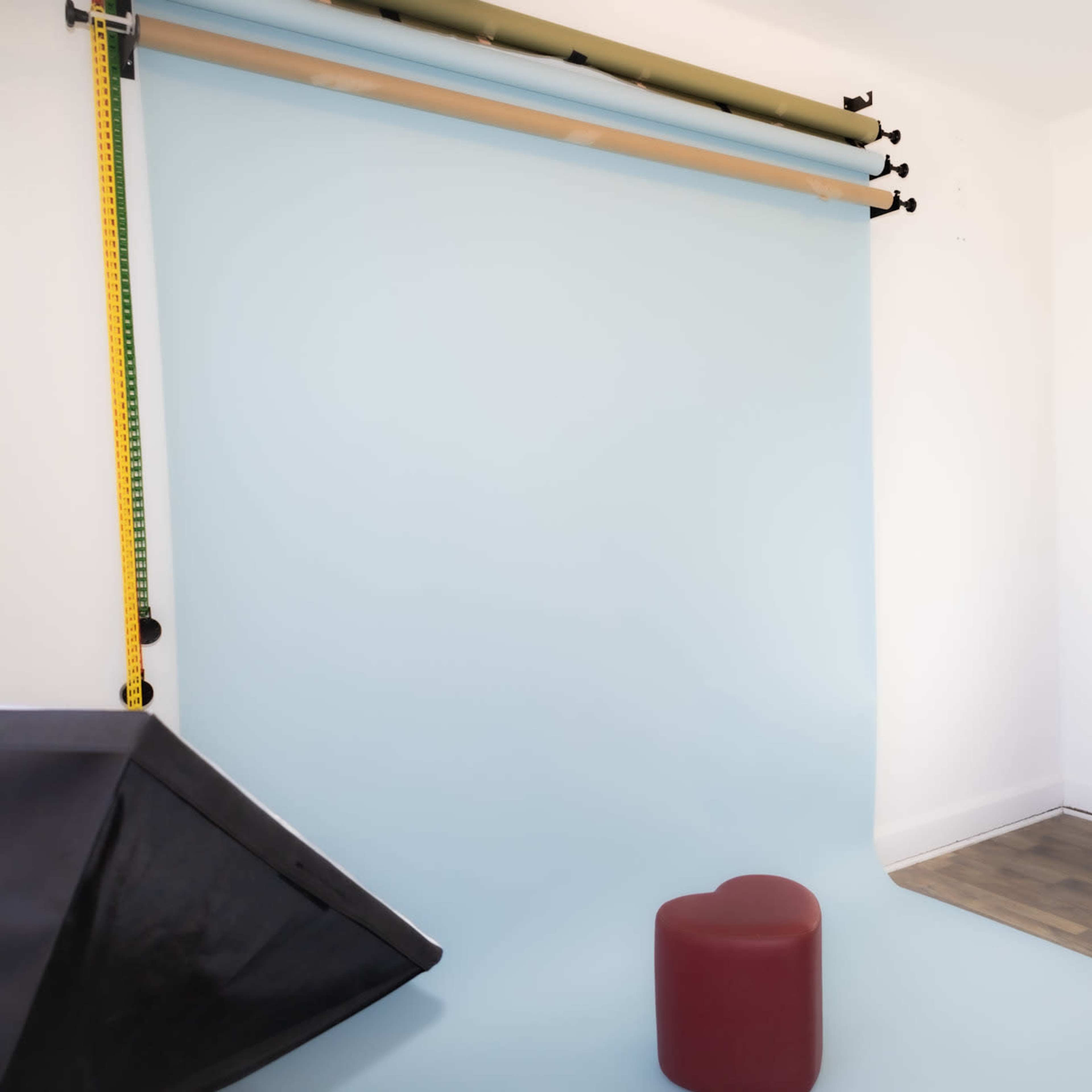 A photography studio with a light blue backdrop, a red heart-shaped stool, and a softbox light setup.