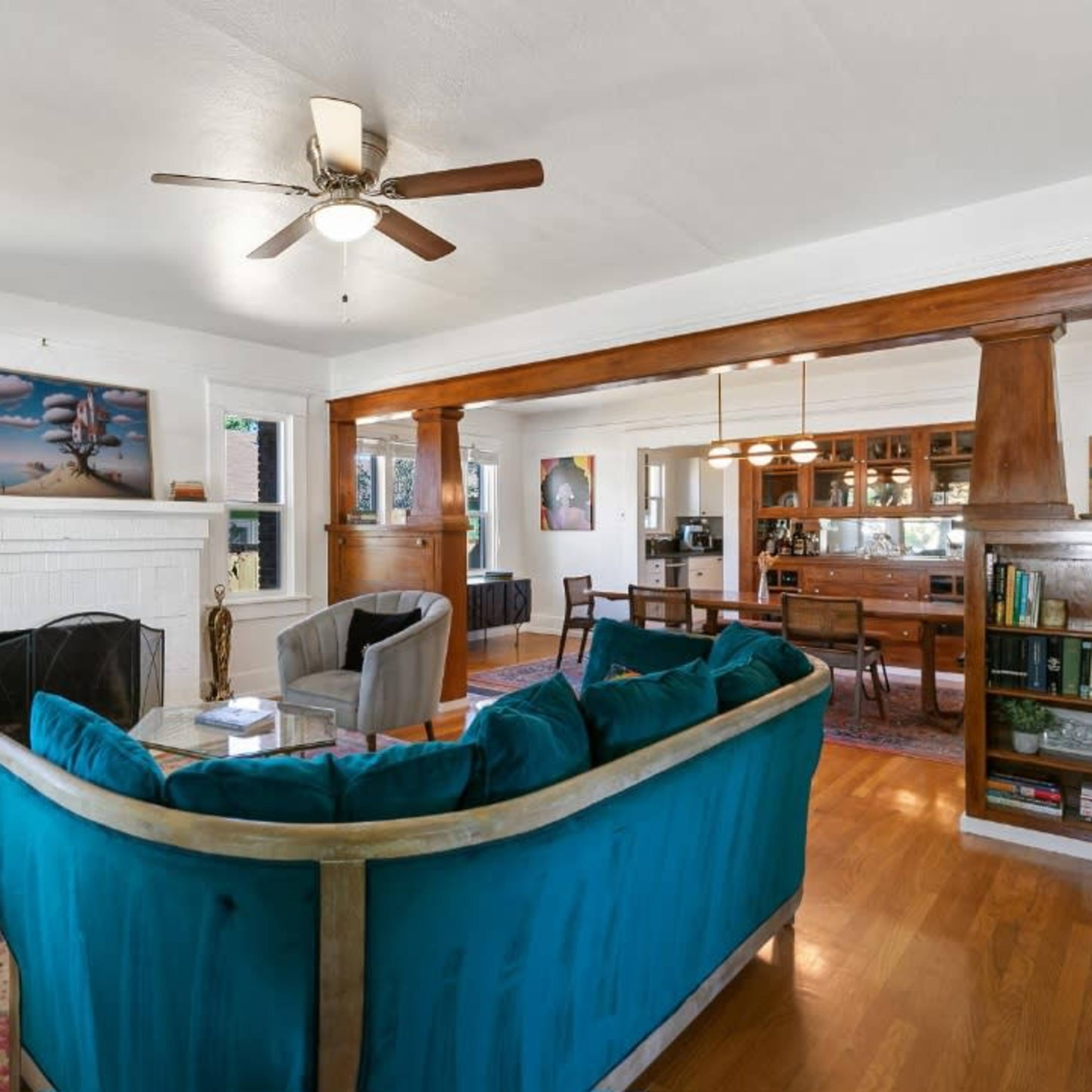 A living room features a turquoise sofa, wooden beams, and a fireplace, with a dining area visible in the background.