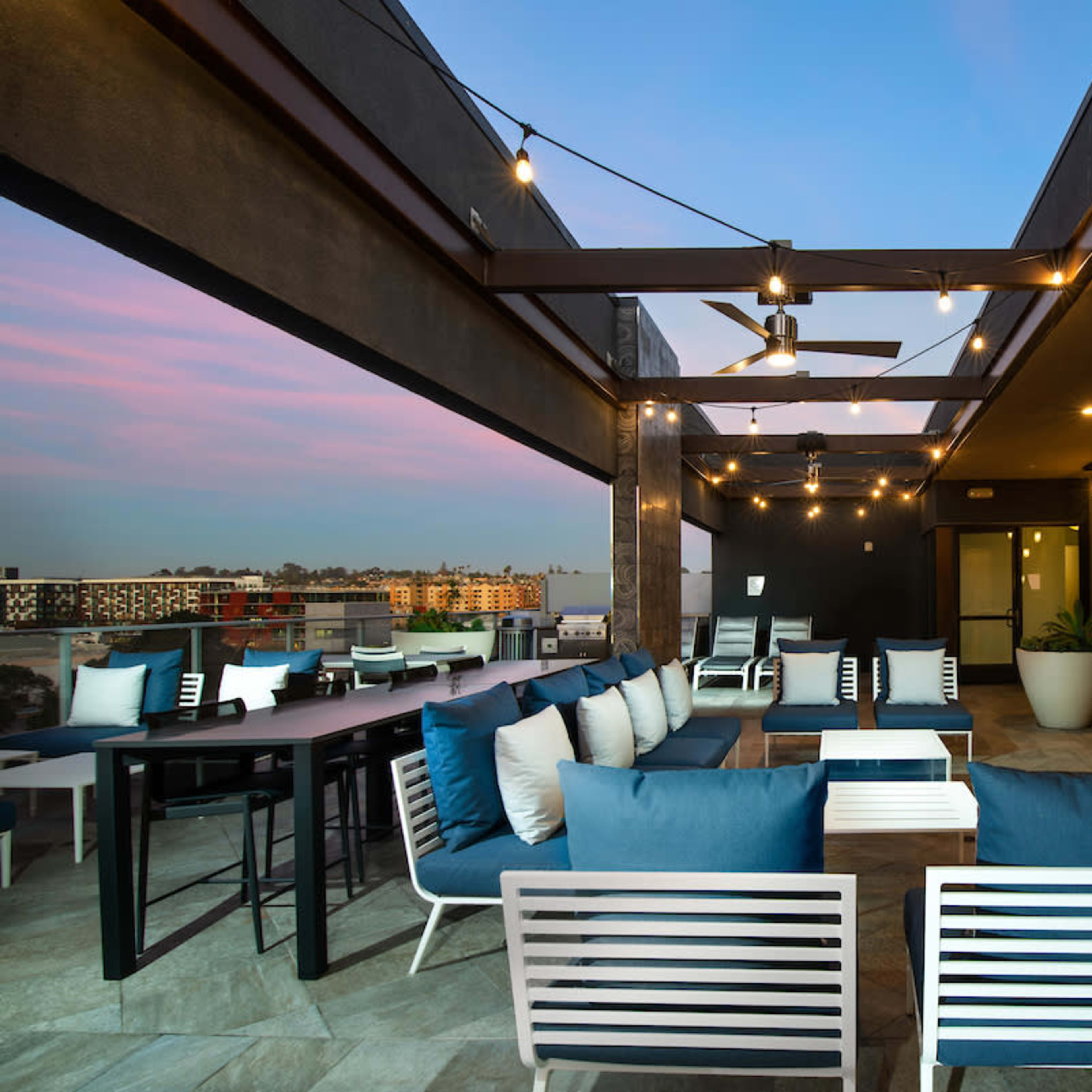 A modern rooftop lounge area with comfortable seating, a television, and decorative lighting.