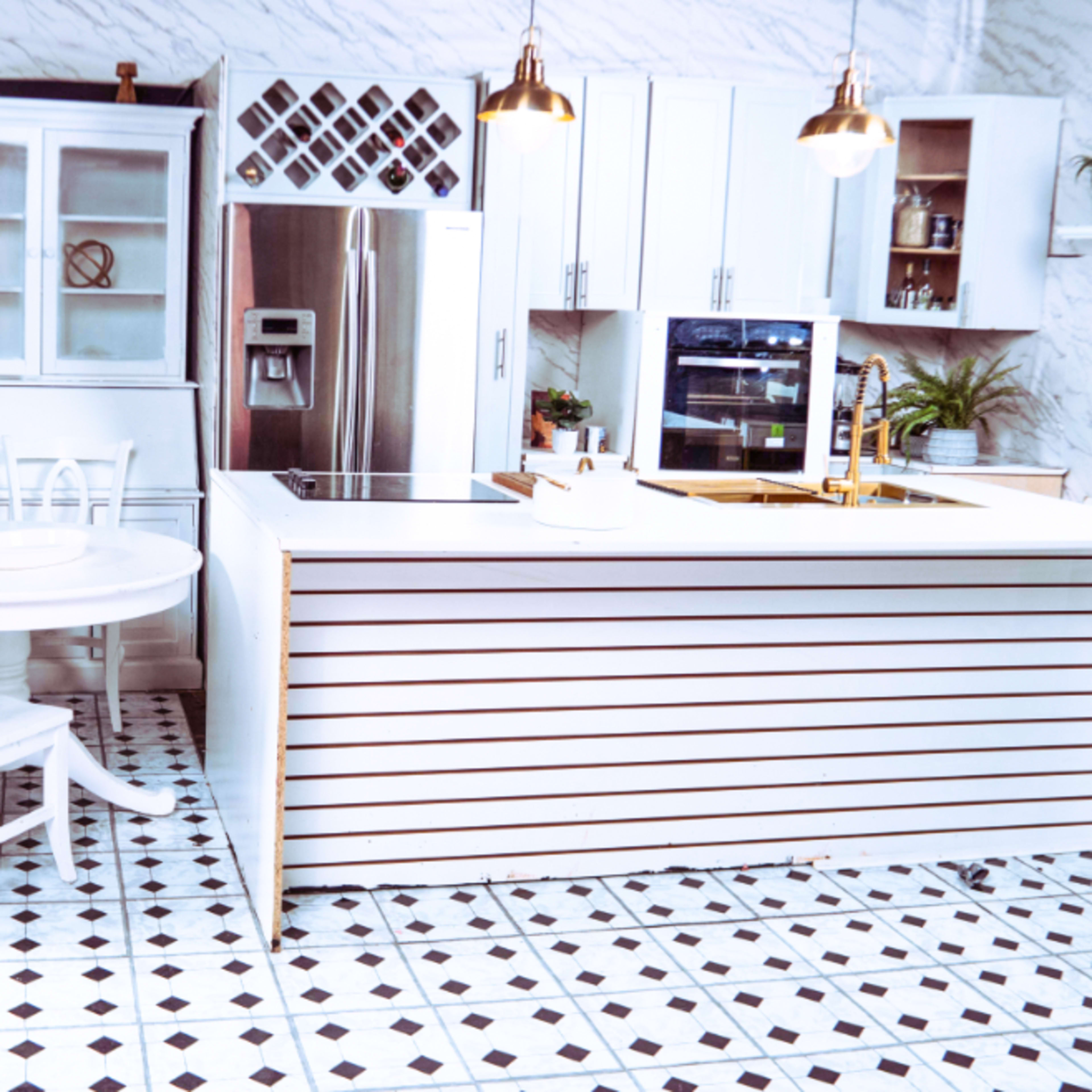A modern kitchen with a white island, cabinets, stainless steel appliances, and a round dining table, all set against a patterned tile floor.
