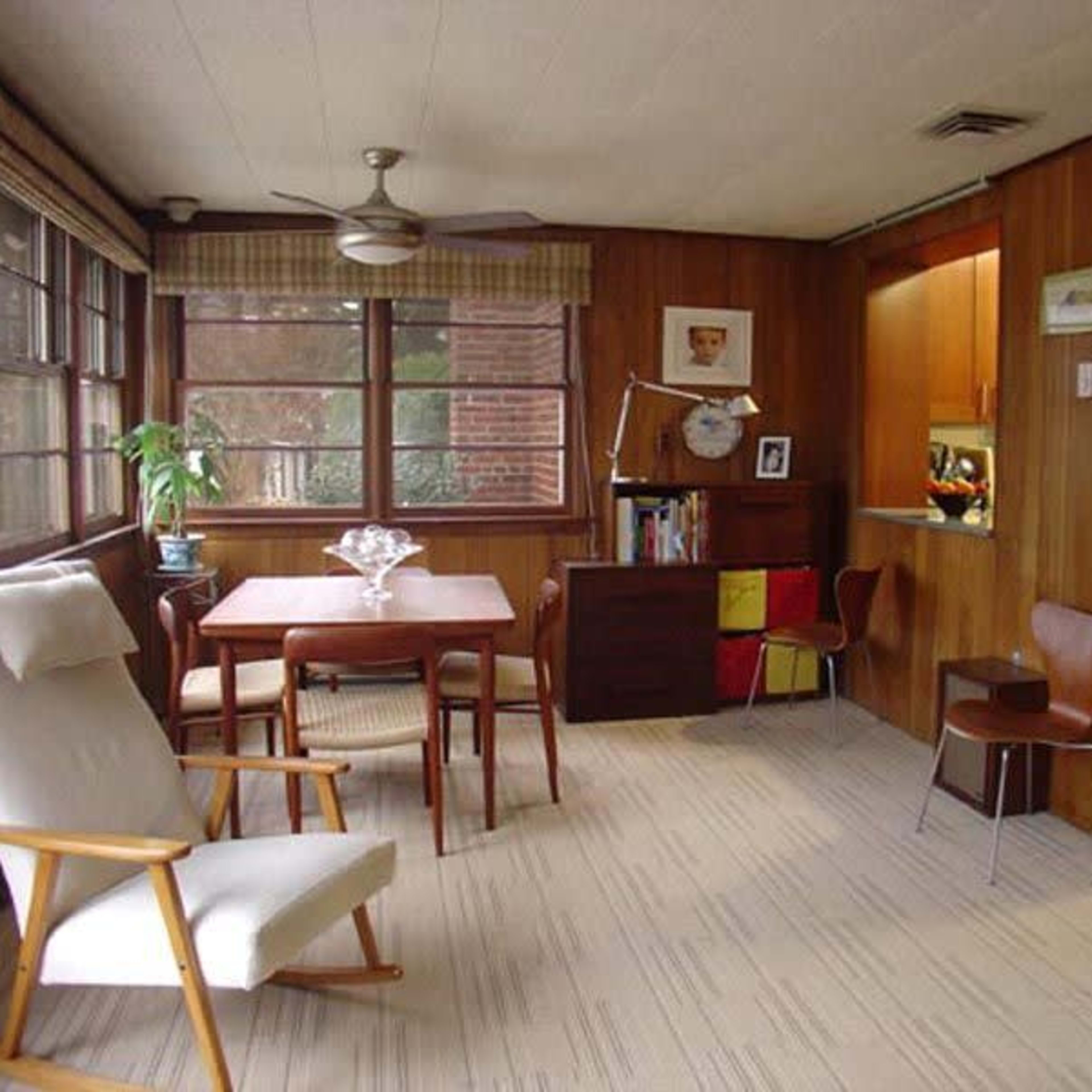 A wooden-paneled room with a dining table, chairs, and a small kitchen area visible in the background.