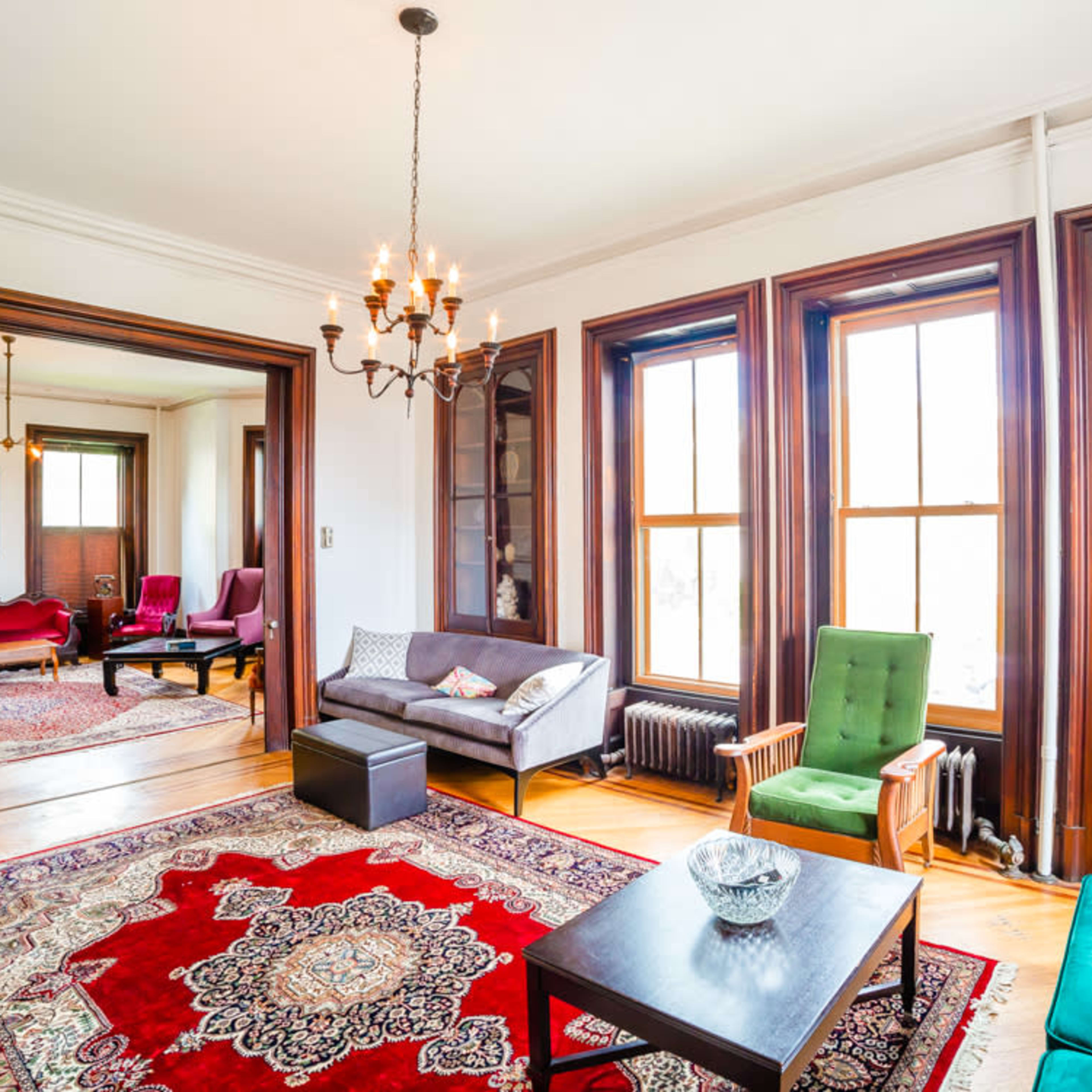 A spacious living room with a decorative red and cream area rug, multiple seating options, and large windows allowing natural light to fill the space.