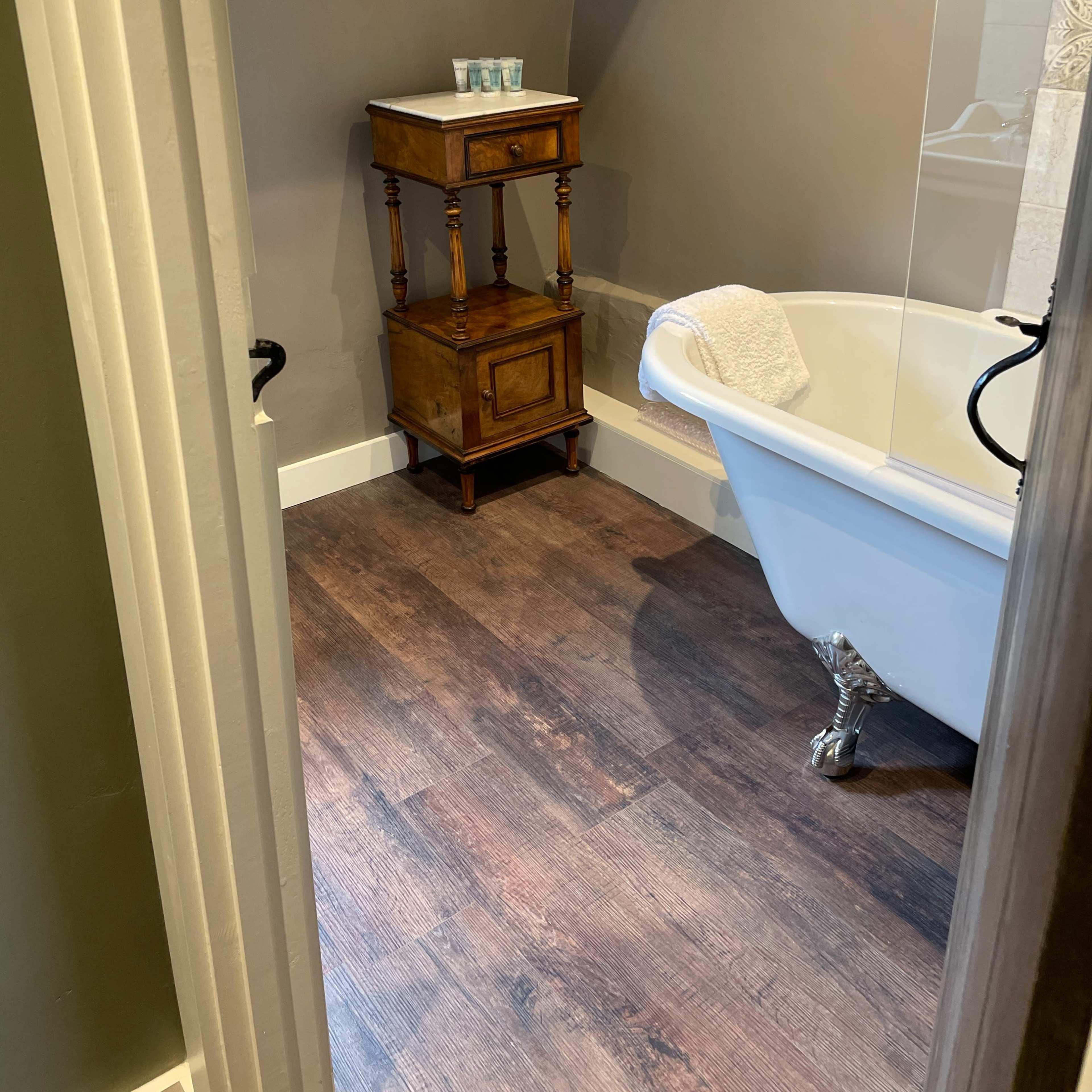 A bathroom featuring a clawfoot bathtub and a wooden side table next to it.