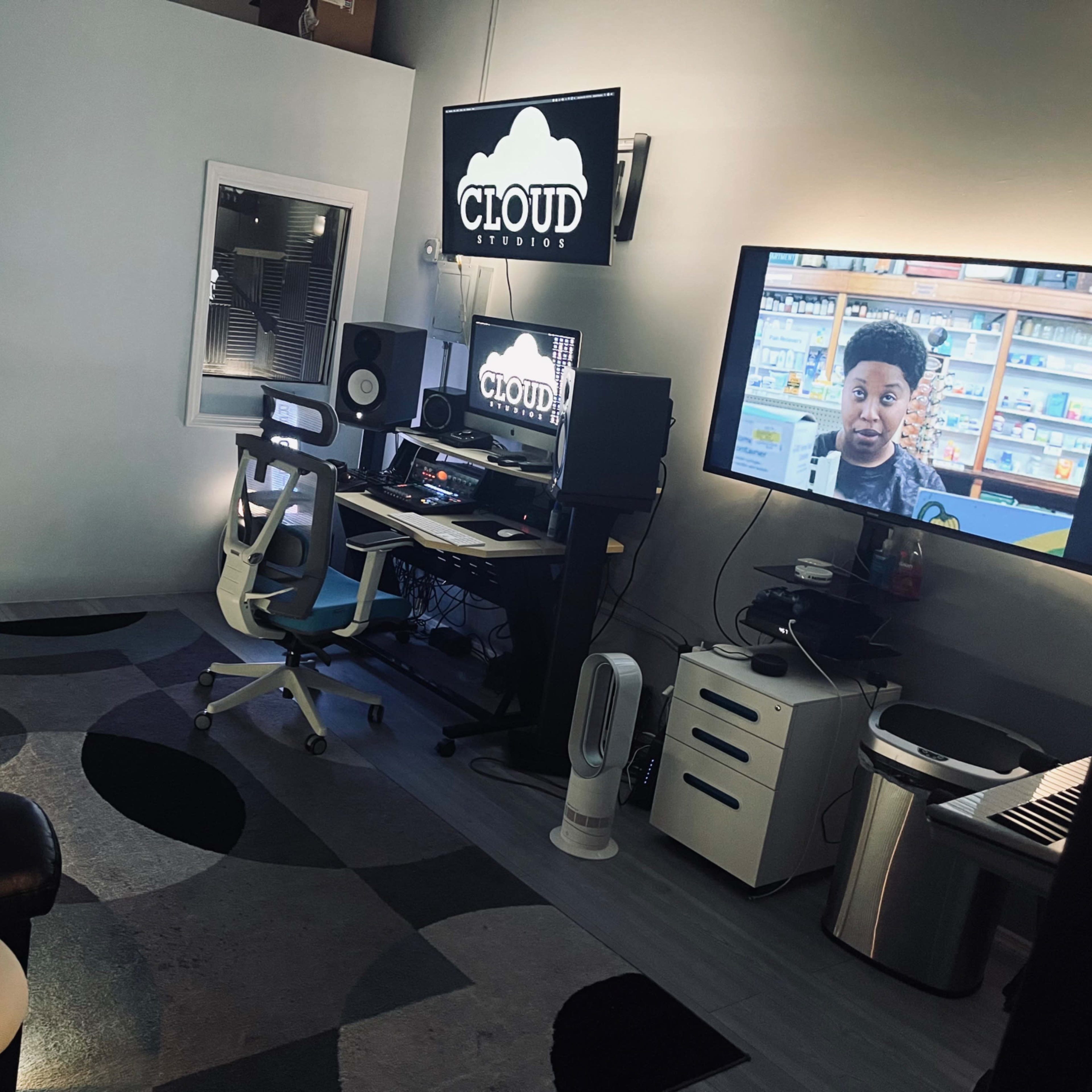 A recording studio with a computer desk, a large screen displaying a video, and a black couch in a room with modern decor.