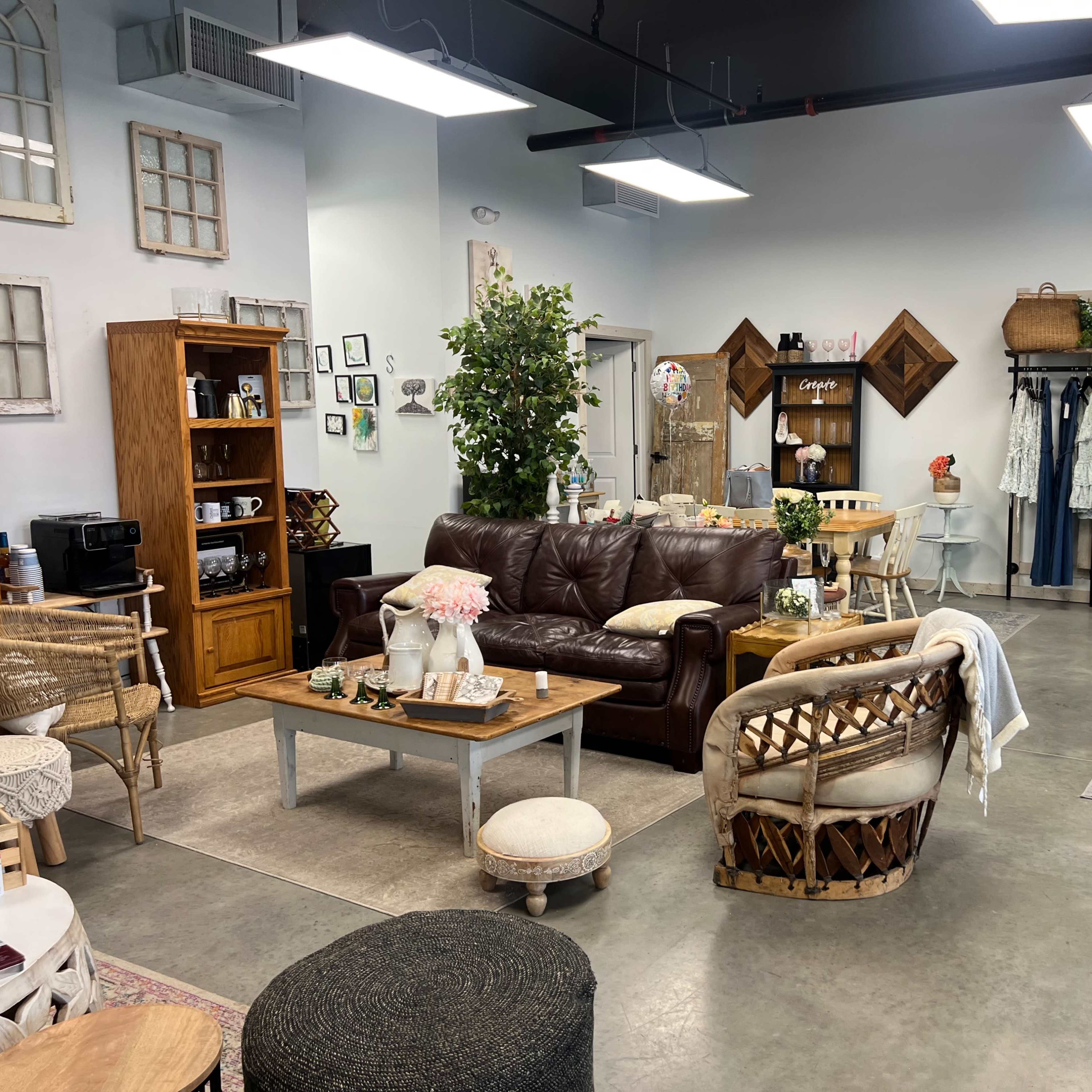 A cozy retail space featuring a brown leather couch, various wooden furniture pieces, decorative items, and a relaxed, inviting atmosphere.