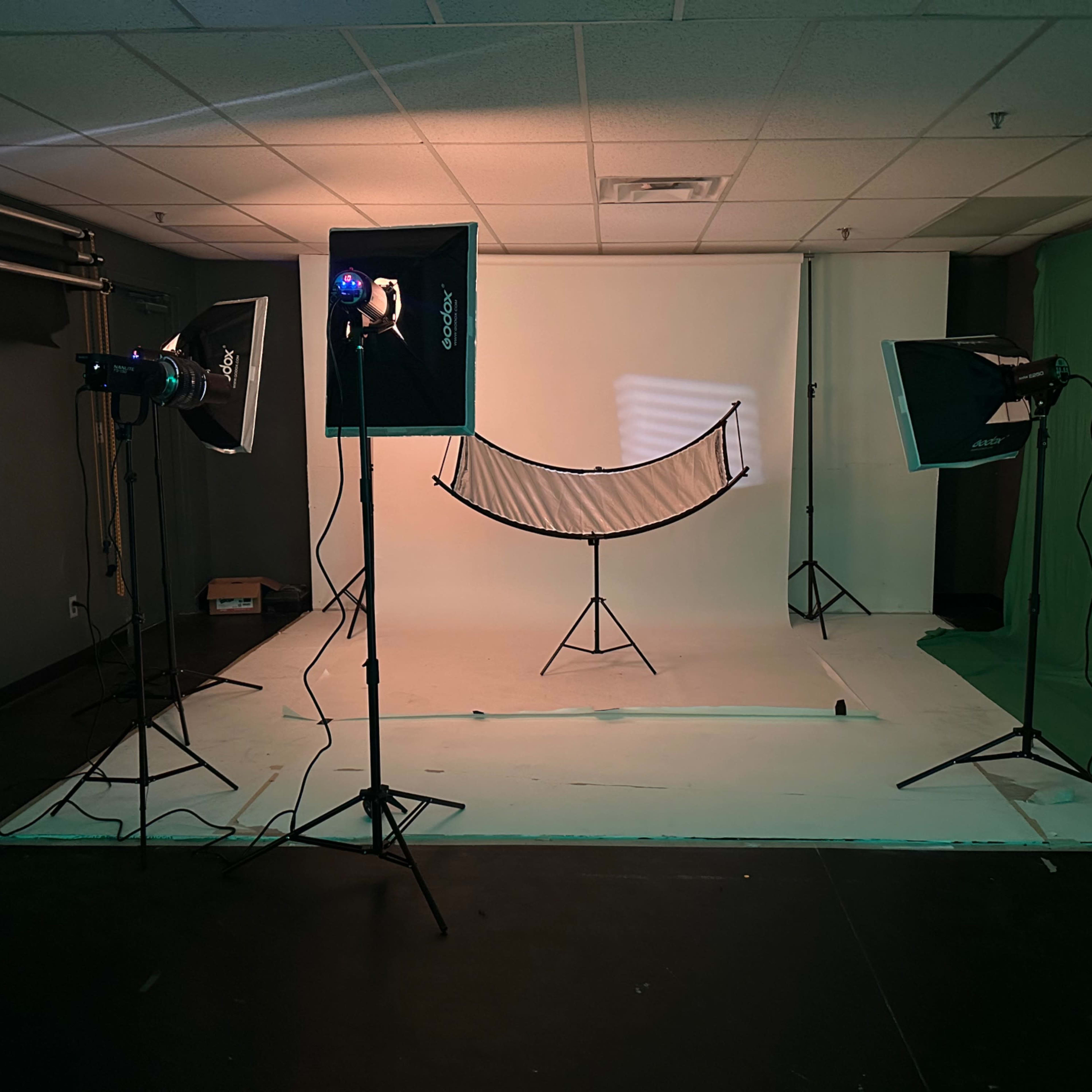 A photography studio setup with two lighting stands, a green backdrop, and a large light diffuser on a tripod in the center against a white background.