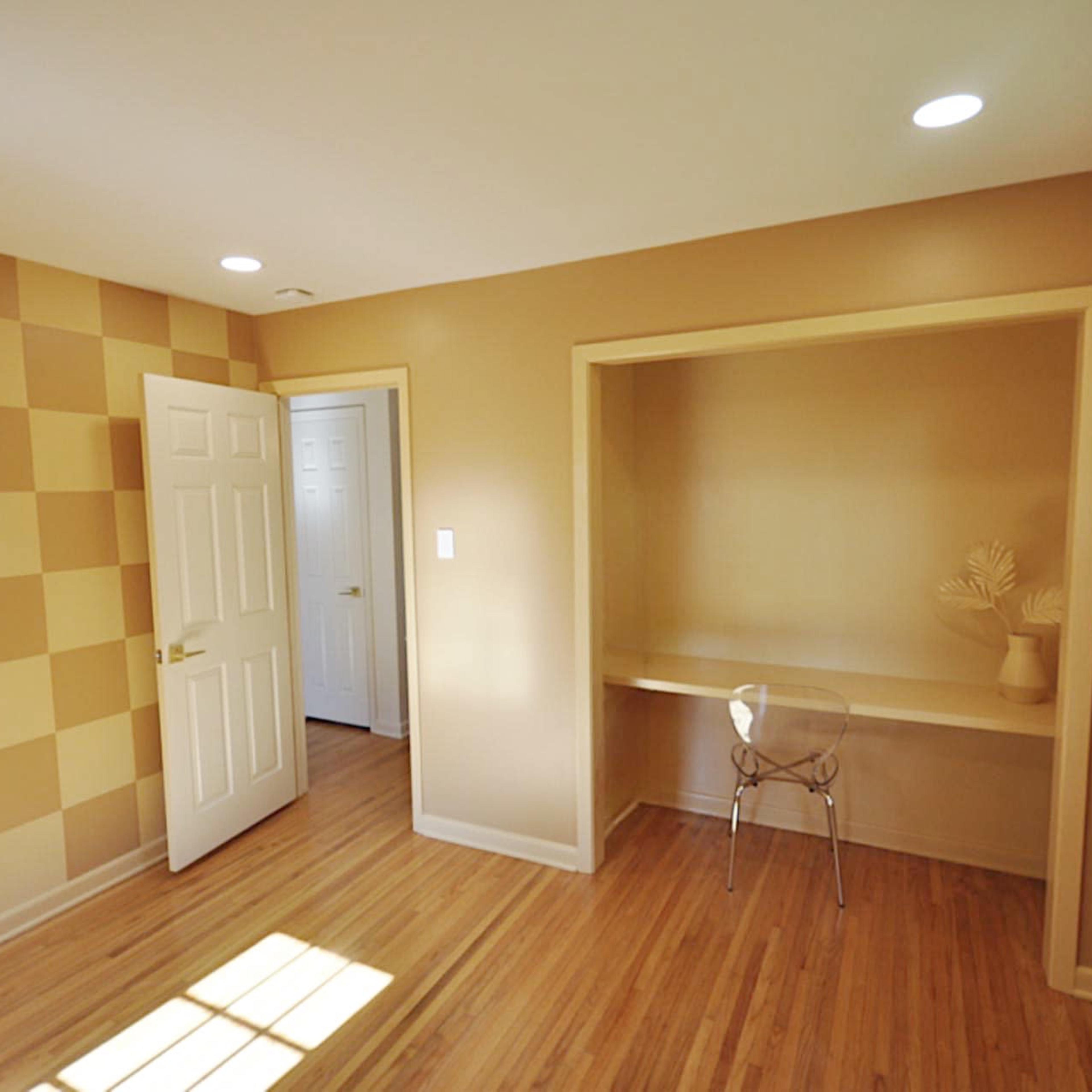 An empty room with a checkered wall design, a door leading to another space, and a built-in nook with a transparent chair.