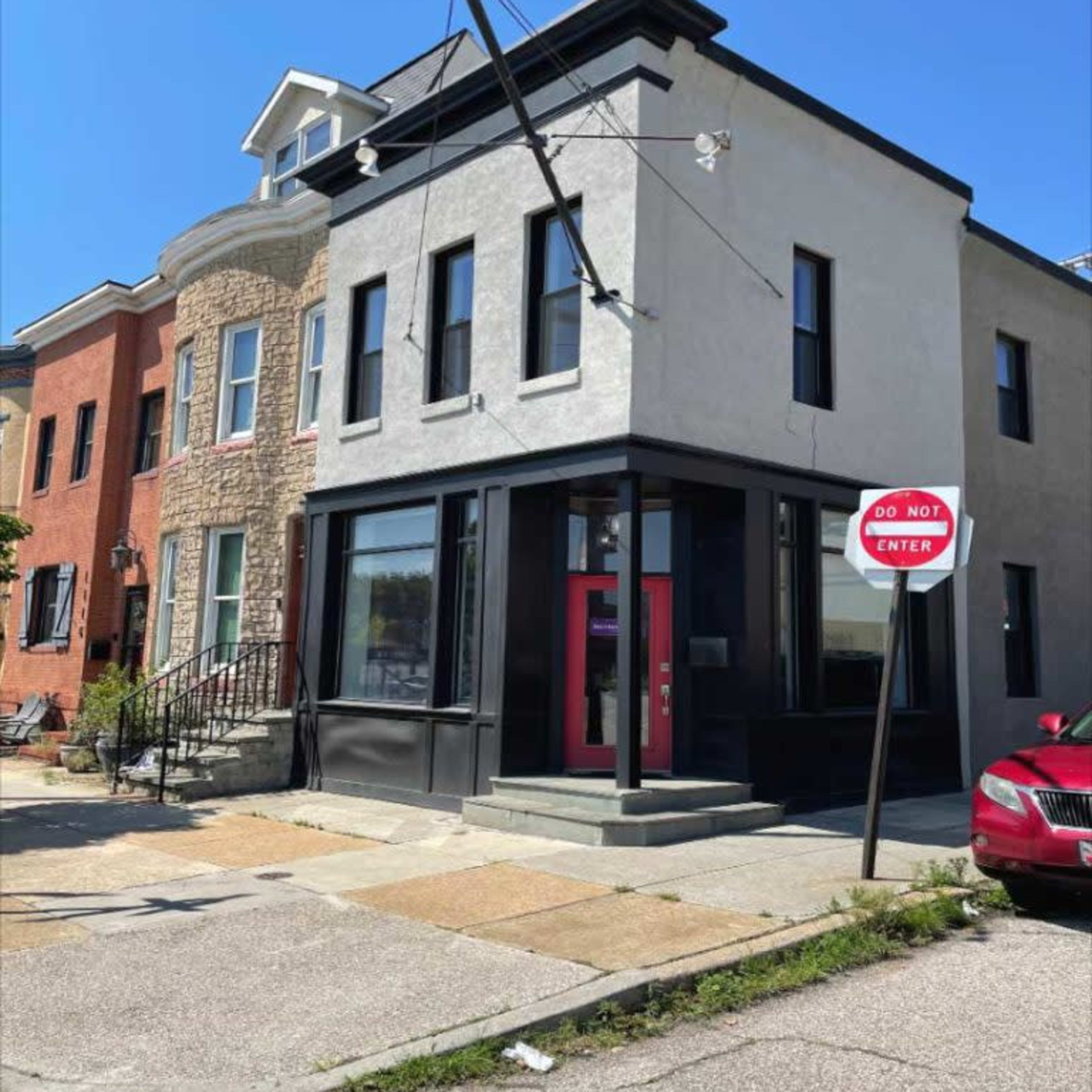 A three-story building with a modern facade, located on a street with a "Do Not Enter" sign and a parked red car.