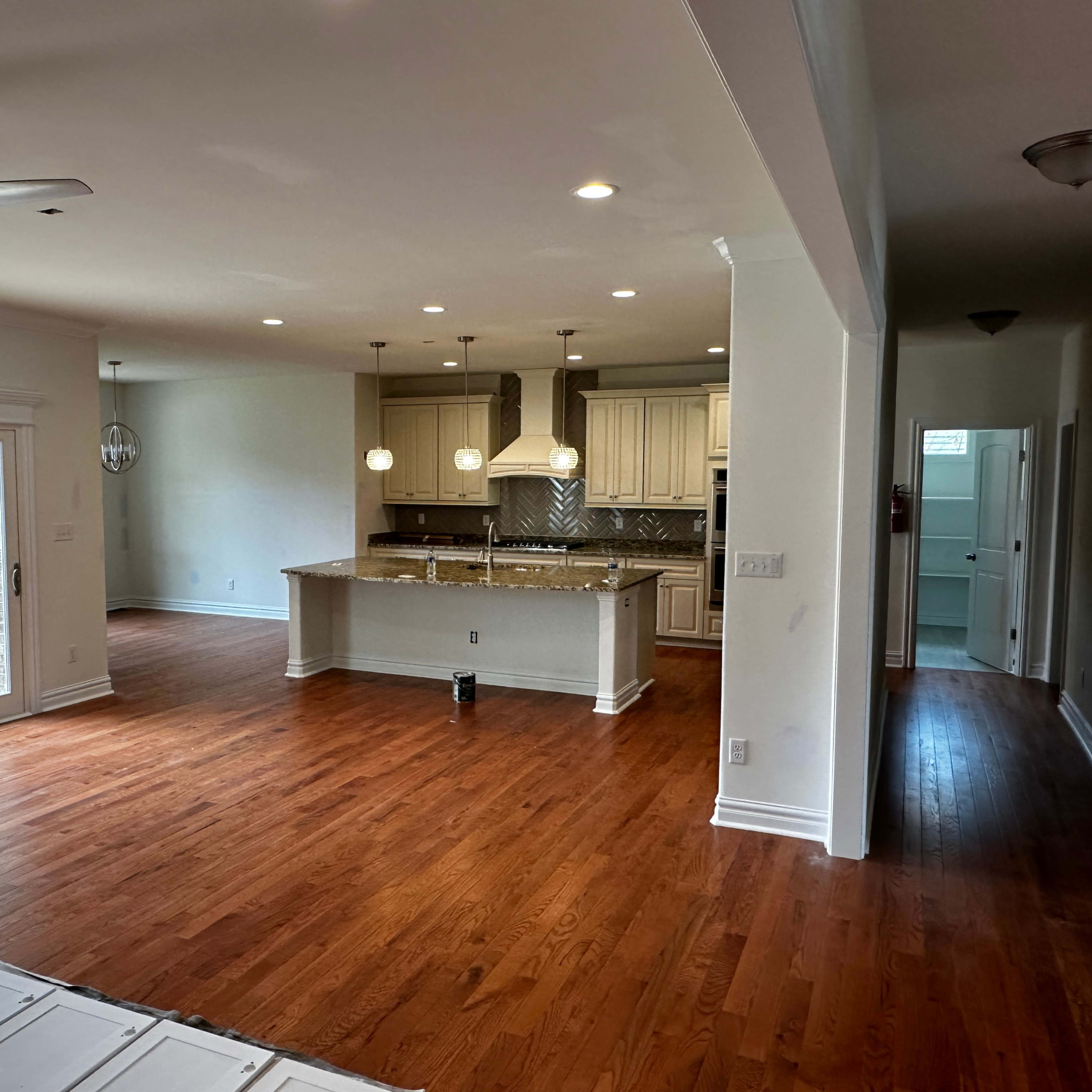 A spacious living area with hardwood floors, a kitchen featuring an island with pendant lights, and a sliding door leading to an outdoor deck.