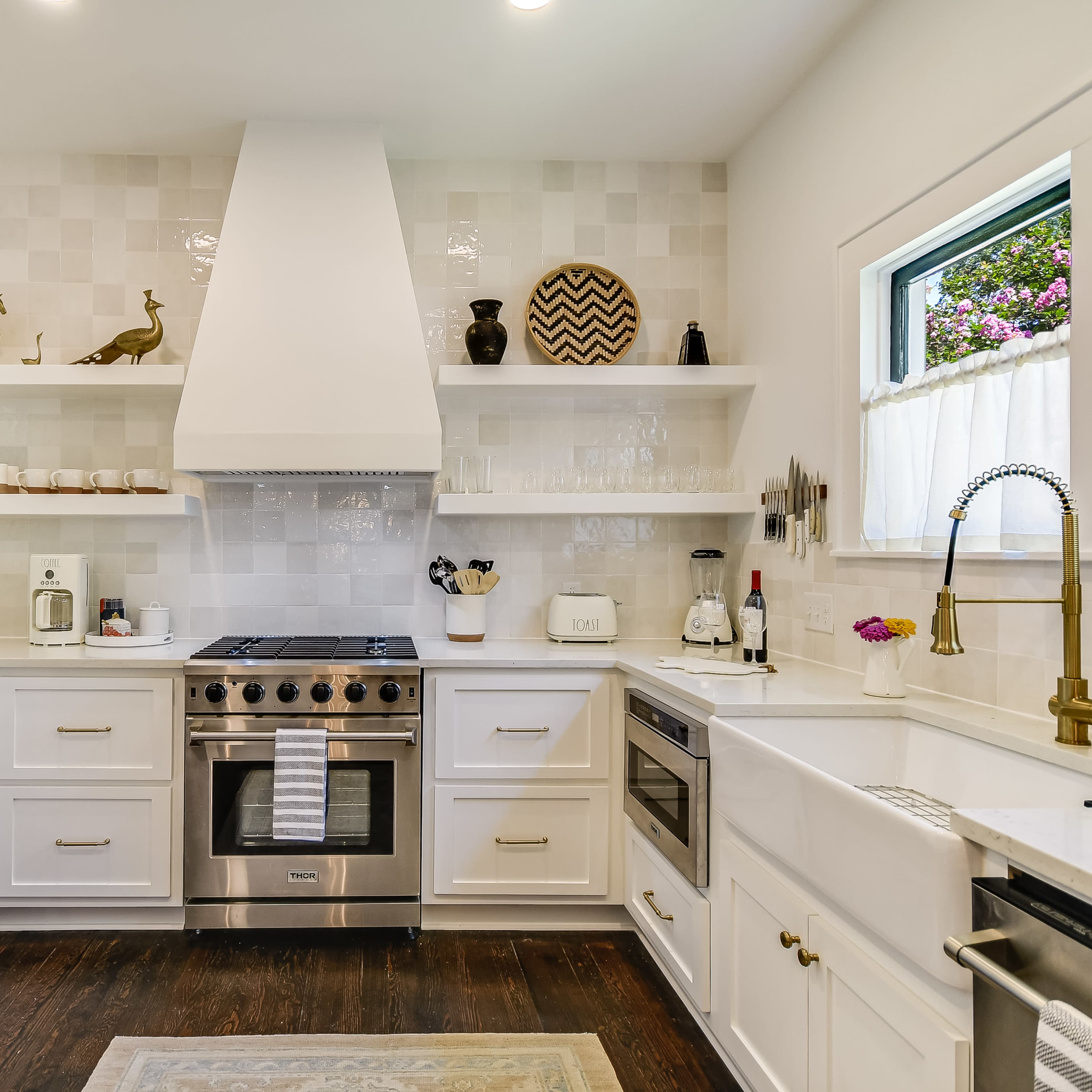 A modern kitchen with white cabinetry, stainless steel appliances, and open shelves displaying decorative items.