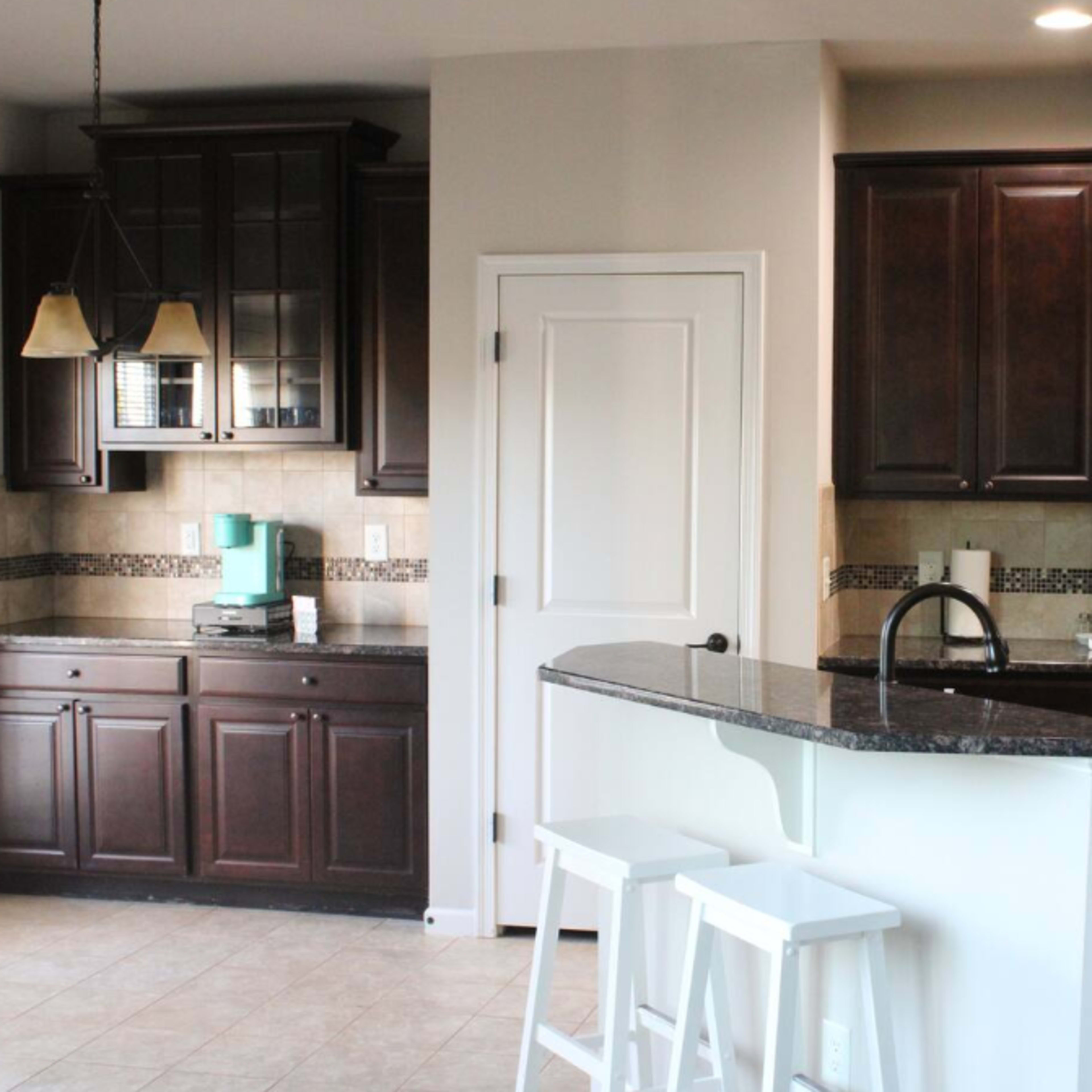 A modern kitchen with dark wood cabinets, stainless steel appliances, and a granite countertop with bar stools.