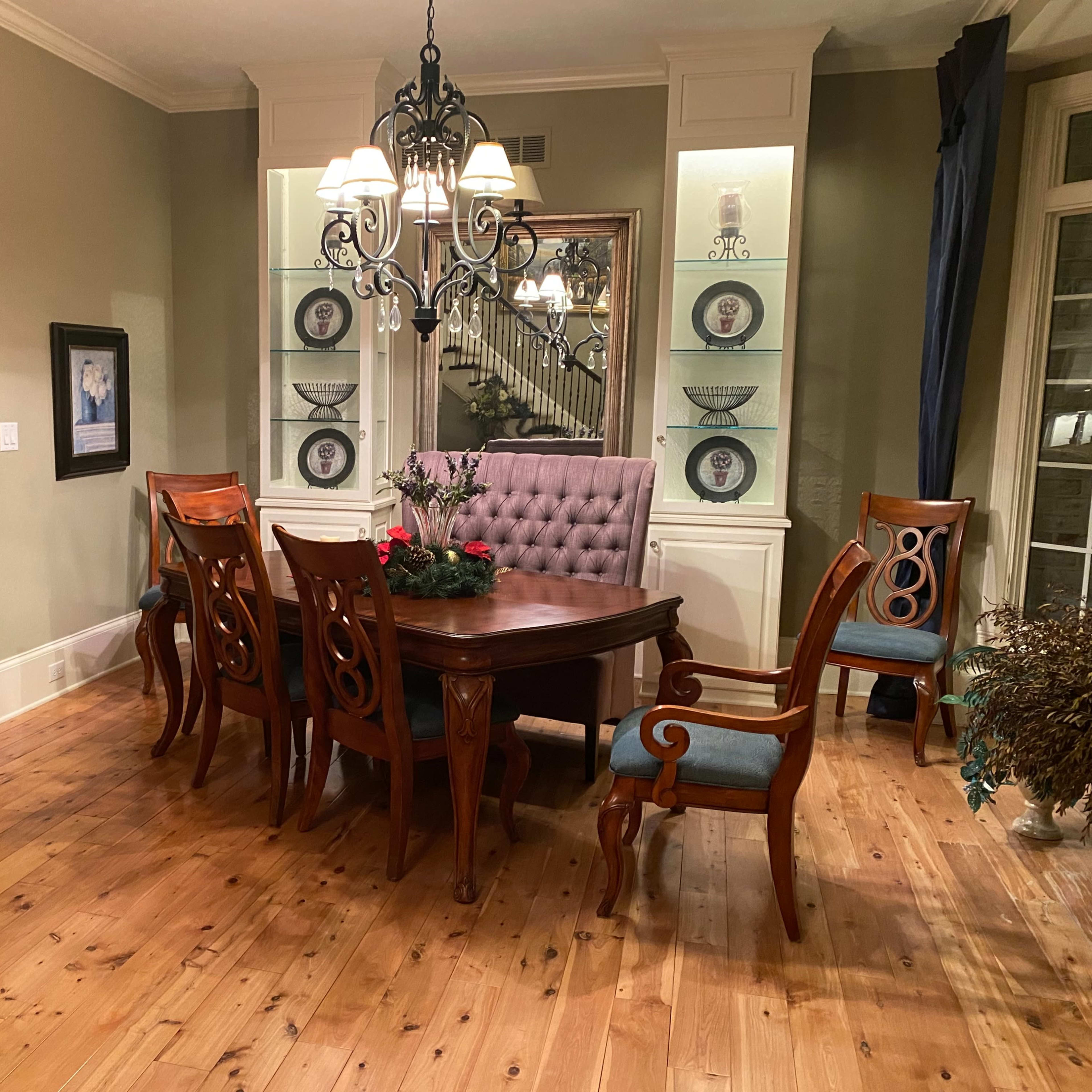 A dining room with a wooden table surrounded by four chairs and a tufted backrest chair, illuminated by a chandelier and accented by decorative wall displays.