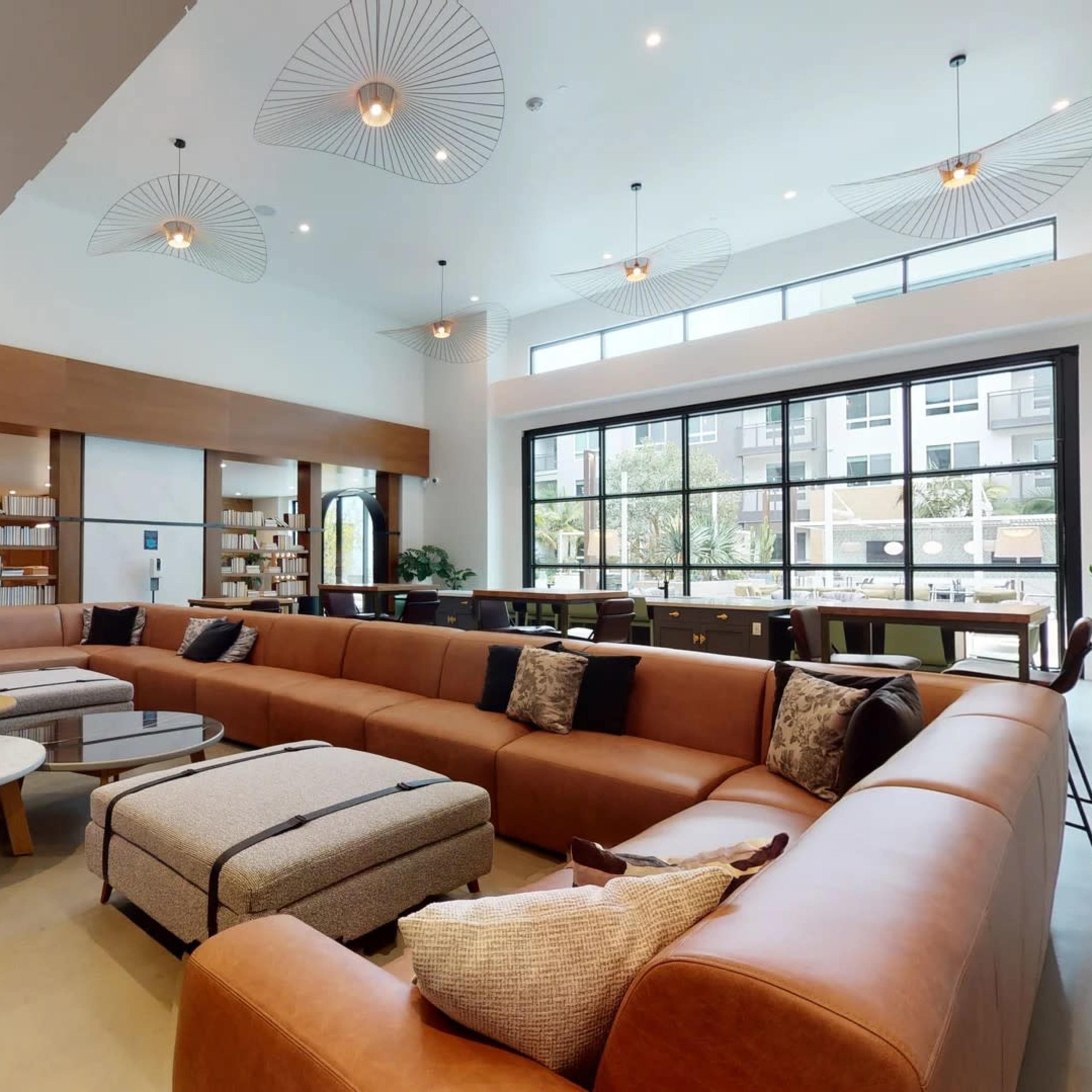 A modern, spacious lounge area featuring a large brown sectional sofa, coffee tables, and ample natural light from large windows.