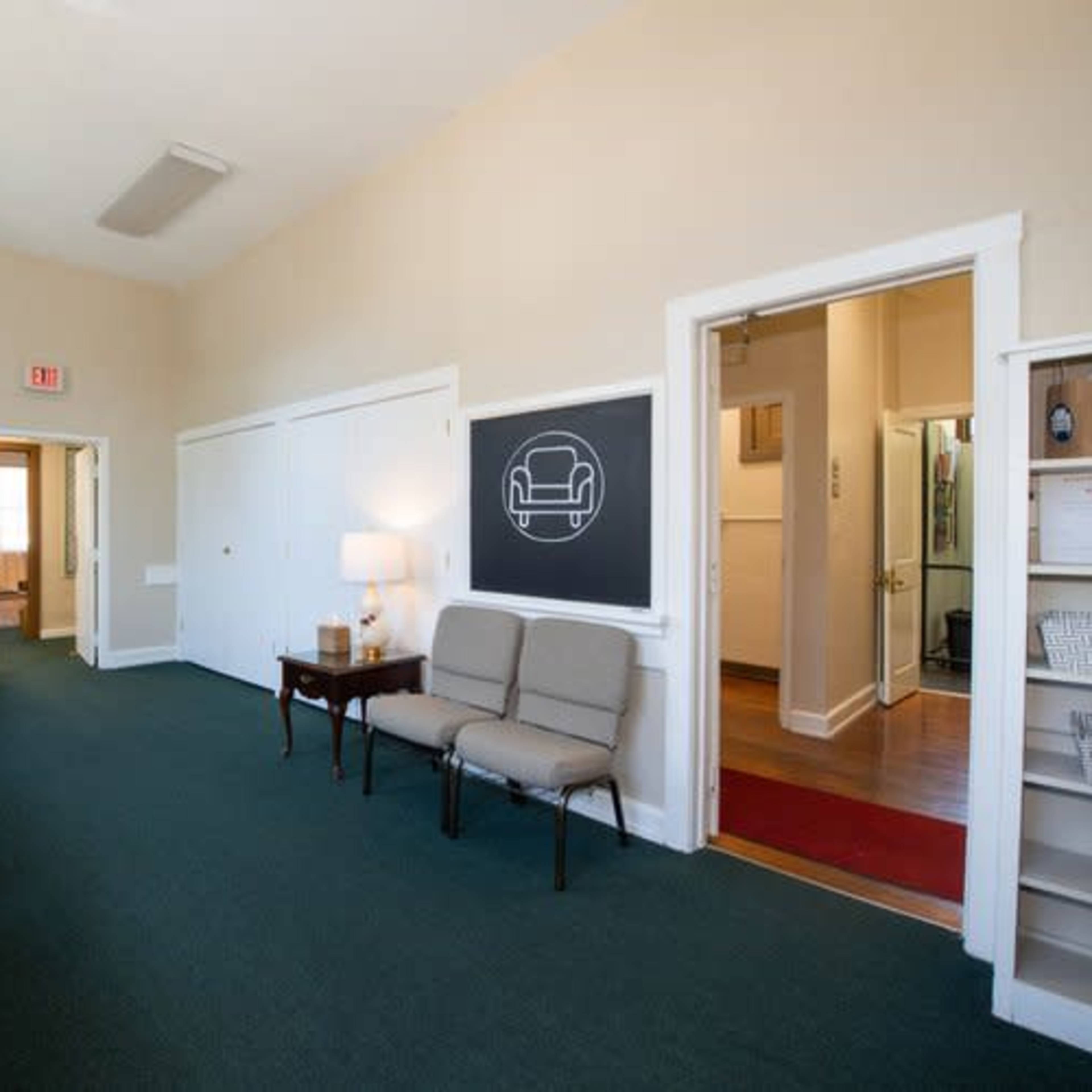 A waiting area with a couch, two chairs, a lamp, and a wall featuring a chalkboard.