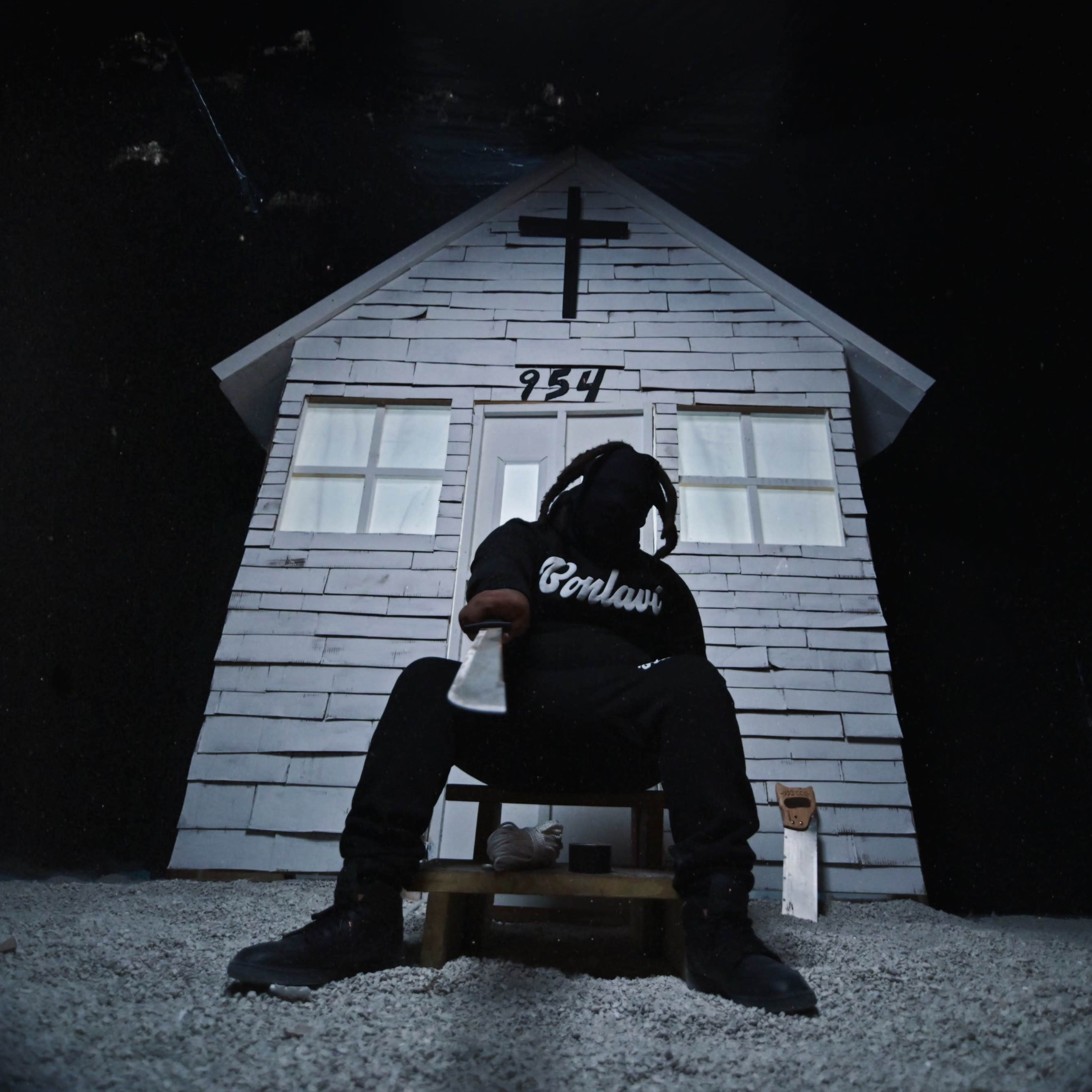 A figure in dark clothing sits on a wooden stool in front of a small, white house with a cross and the number 254 on it.