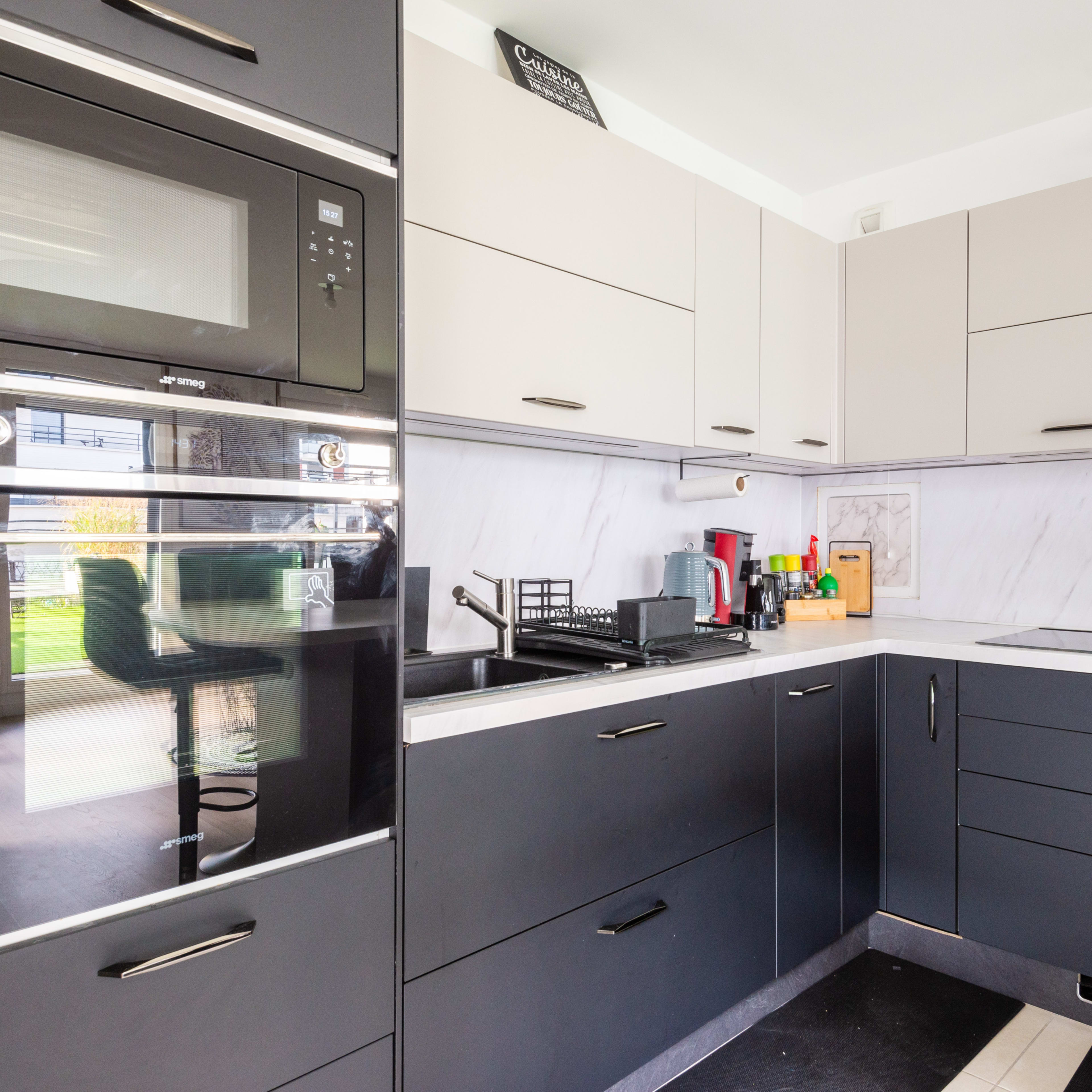 A modern kitchen with black and gray cabinetry, a built-in oven, and a window revealing an outdoor view.