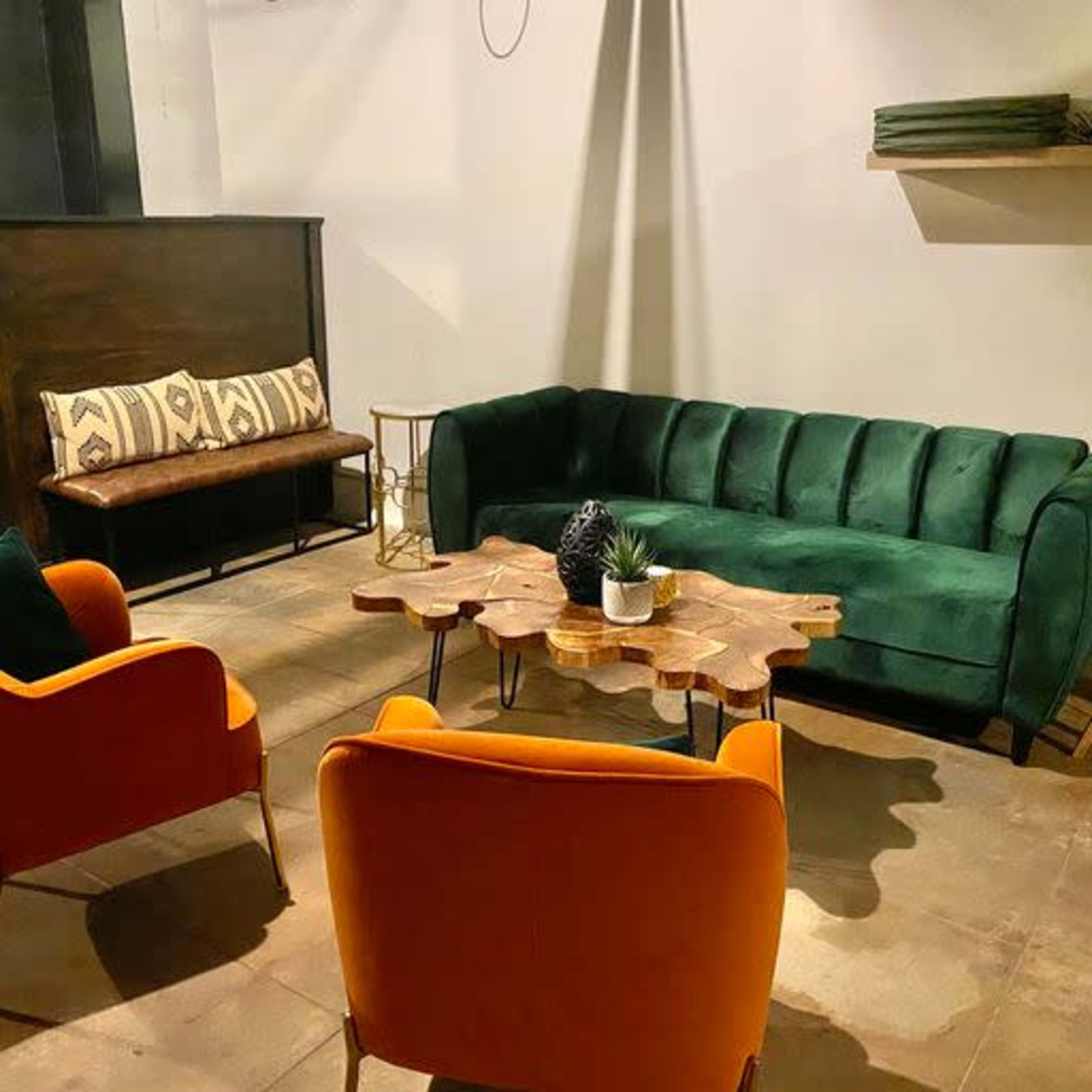 A small lounge area featuring a green sofa, two orange chairs, a wooden coffee table, and a patterned bench along the wall.