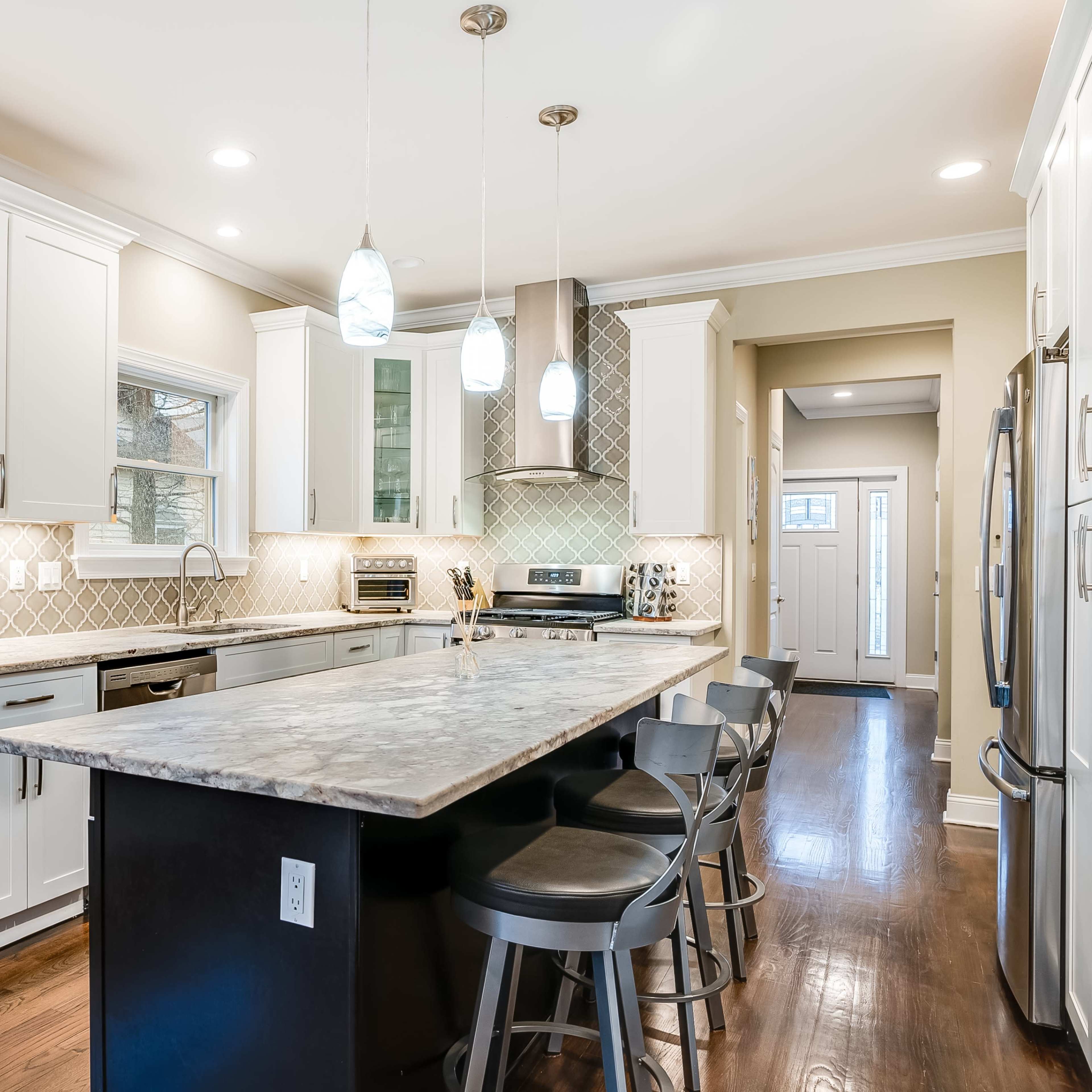 A modern kitchen features white cabinetry, gray countertops, stainless steel appliances, and a large island with seating.