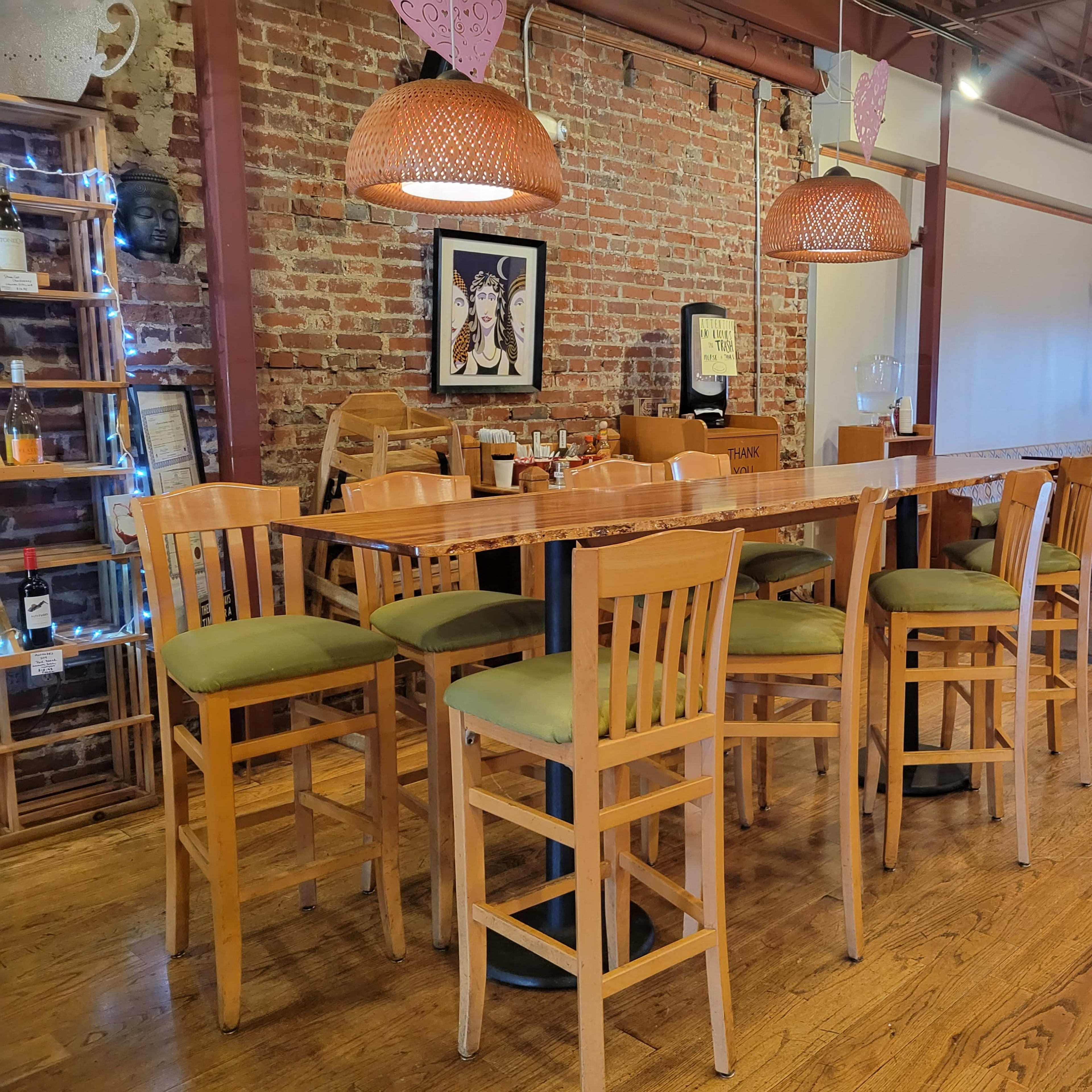A rustic interior of a restaurant with a long wooden bar and seating for several patrons, surrounded by exposed brick walls and decorative light fixtures.