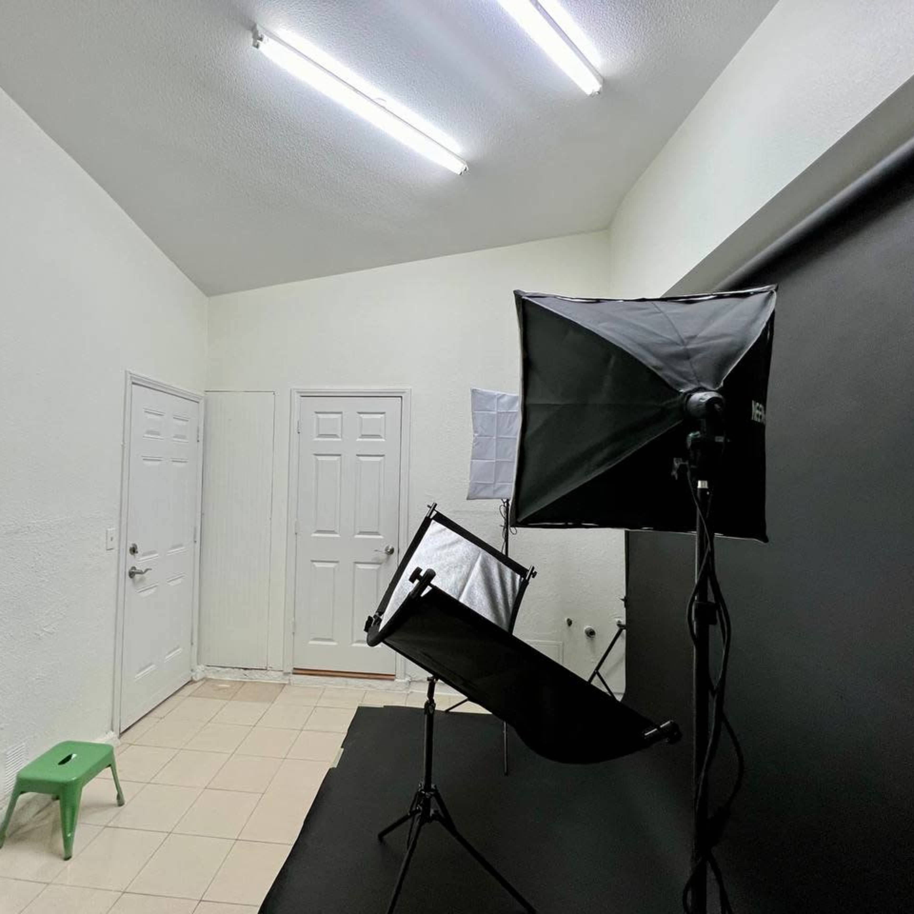 A small studio space with a black backdrop, two softboxes, a green stool, and a door leading to another area.