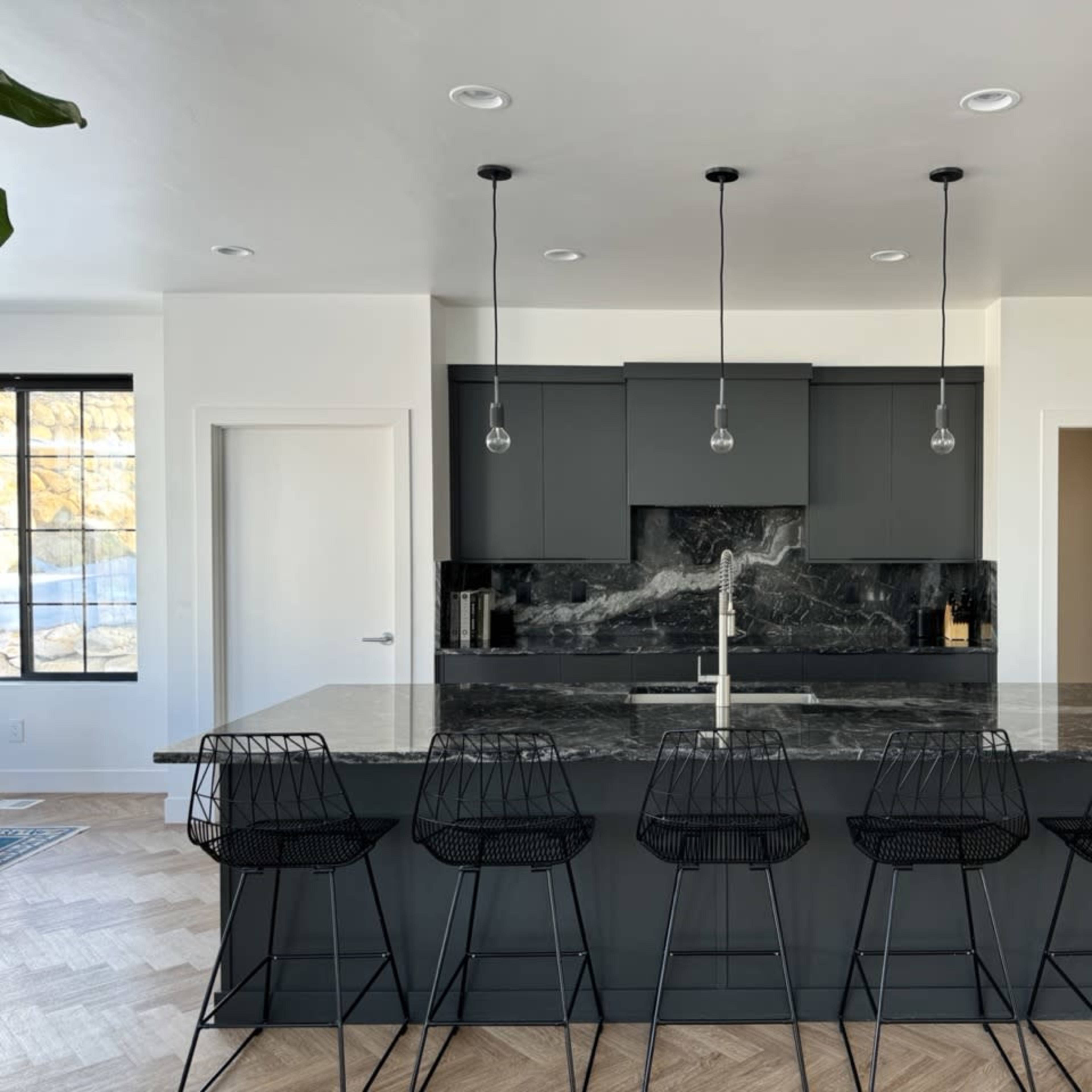 A modern kitchen features a large island with a dark marble countertop and five black wire bar stools.
