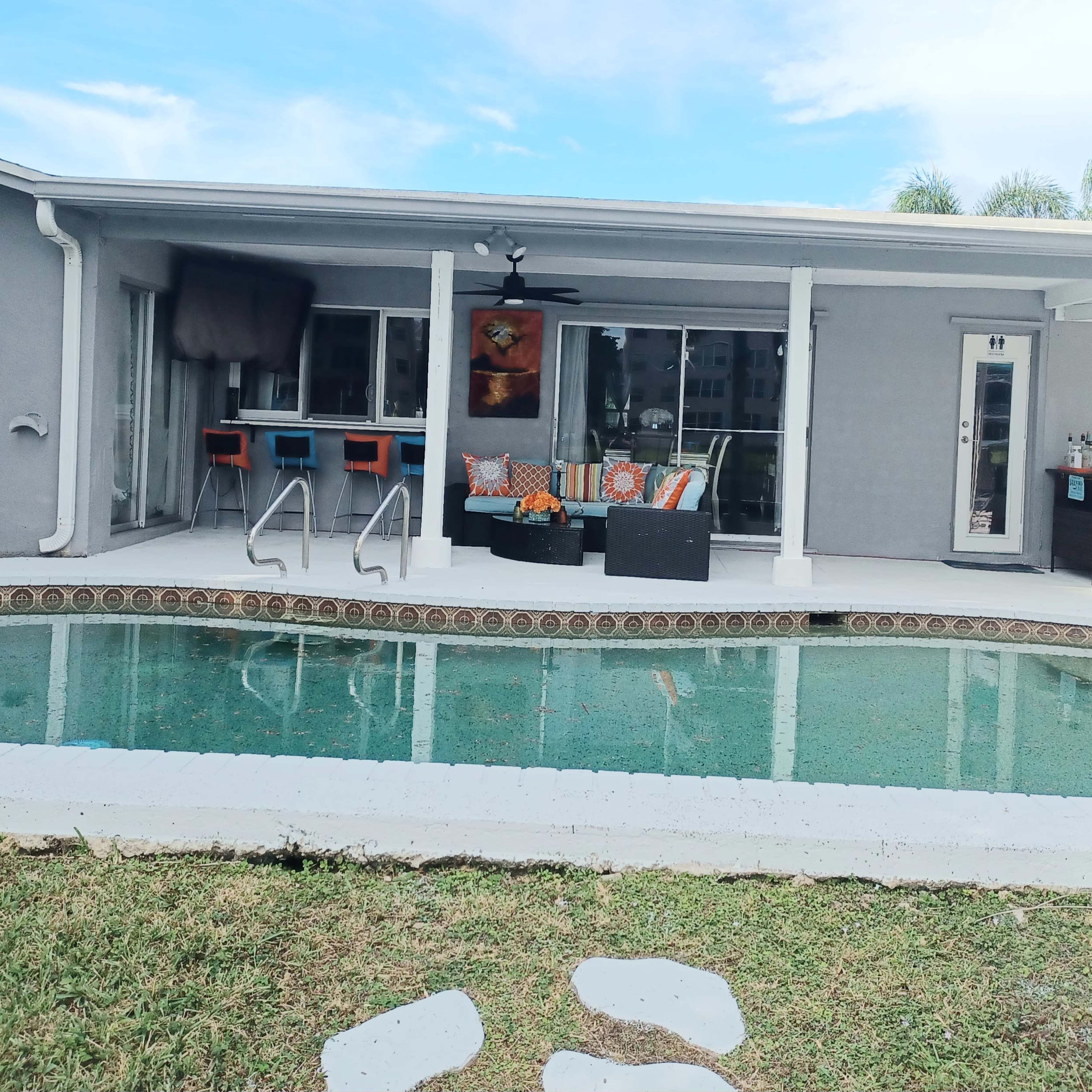 A backyard with a swimming pool, patio furniture, and a covered seating area adjacent to a house.